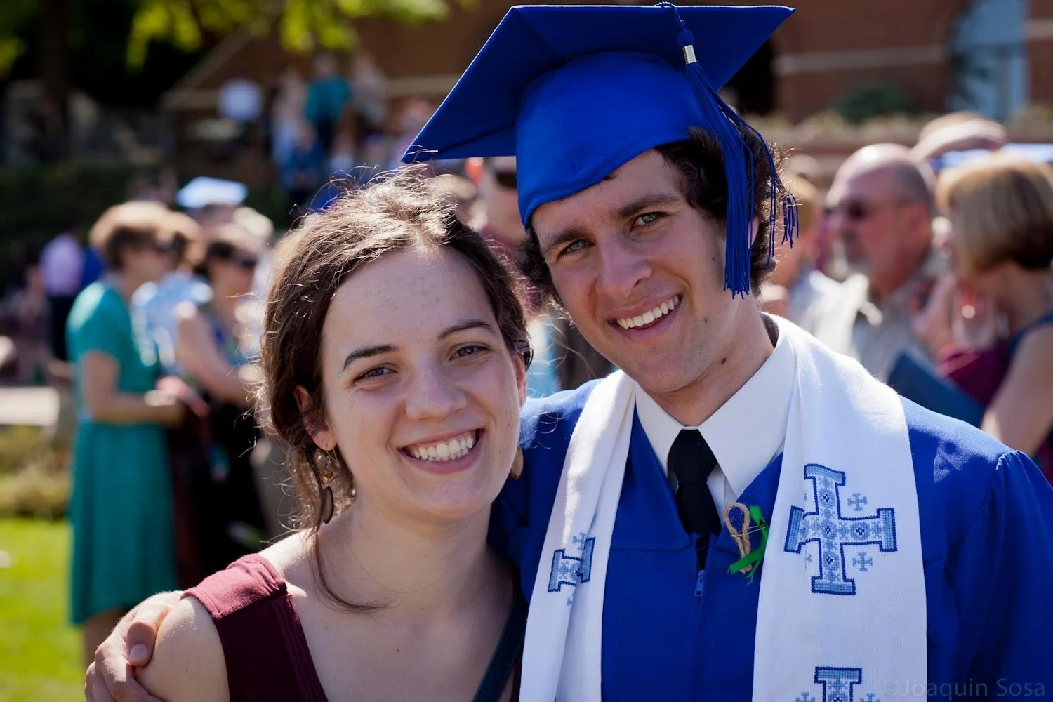 A young woman and a young man in graduation attire smiling and embracing at a graduation ceremony outdoor celebration.
