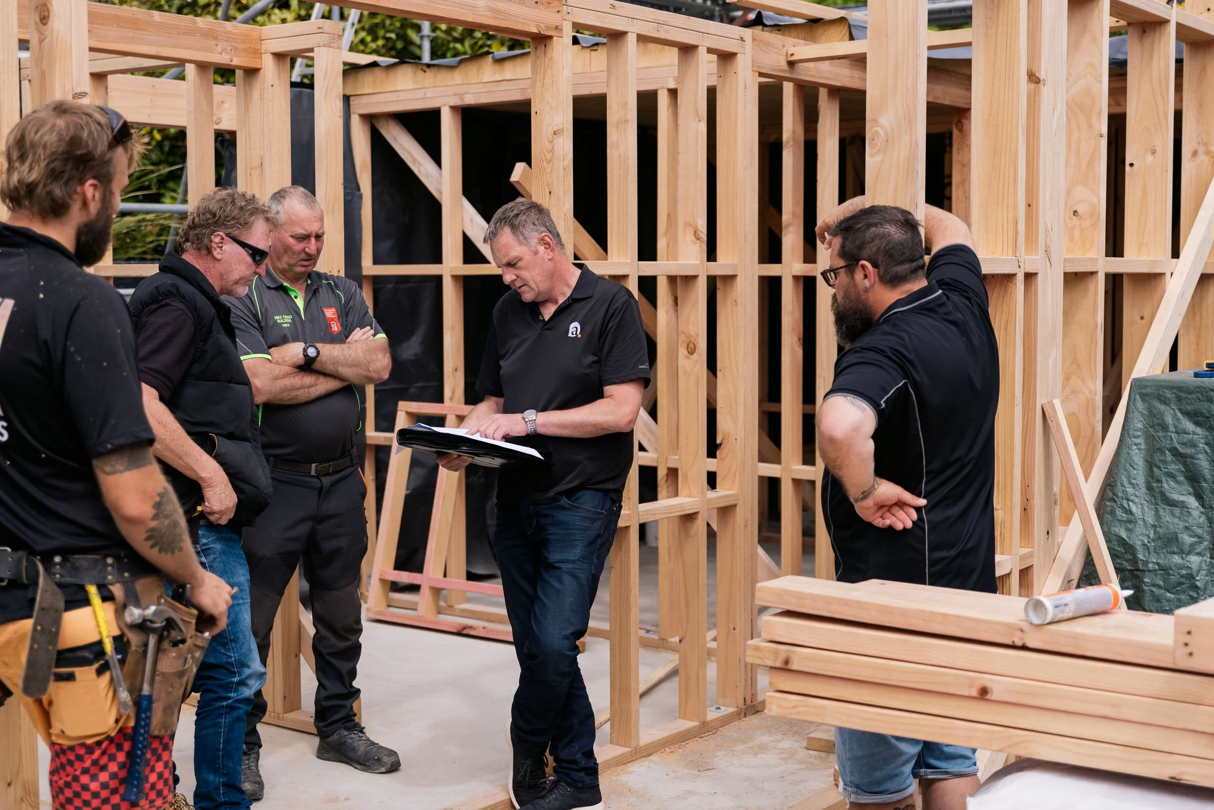 Group of five men discussing a construction project for a wooden building frame at a construction site.