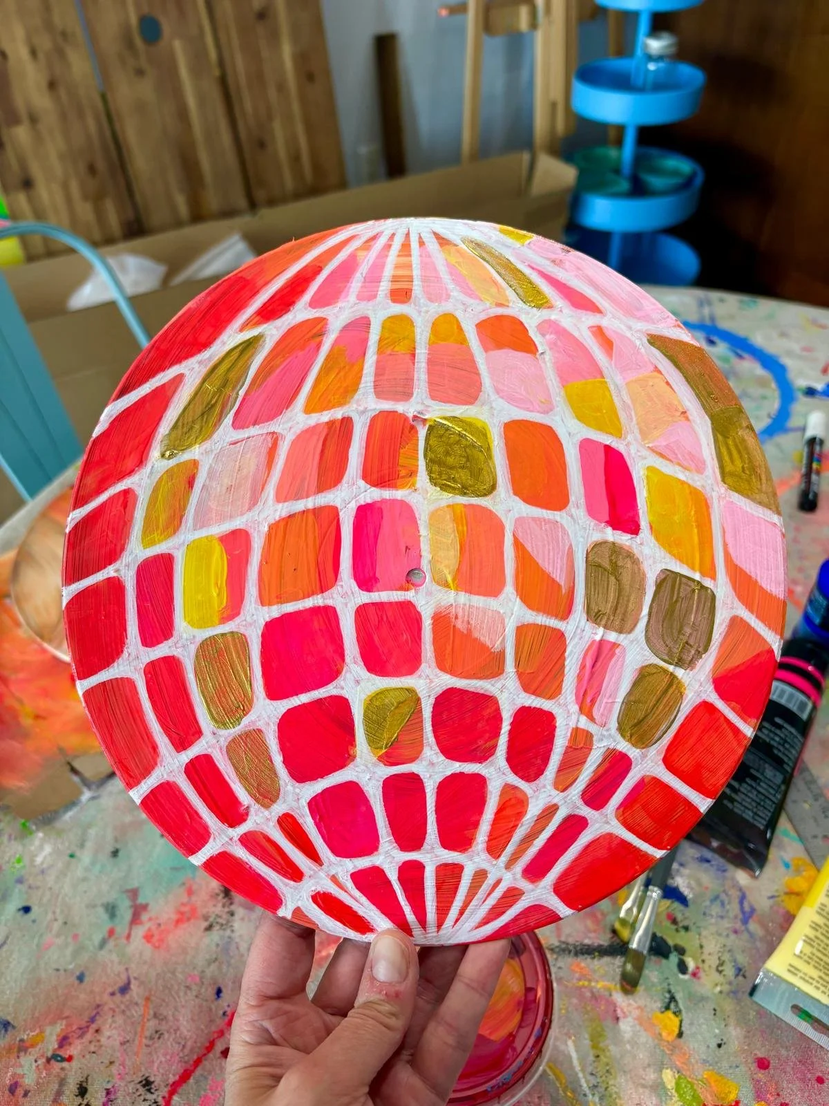 Painted paper lantern with red, pink, gold, and white geometric pattern.