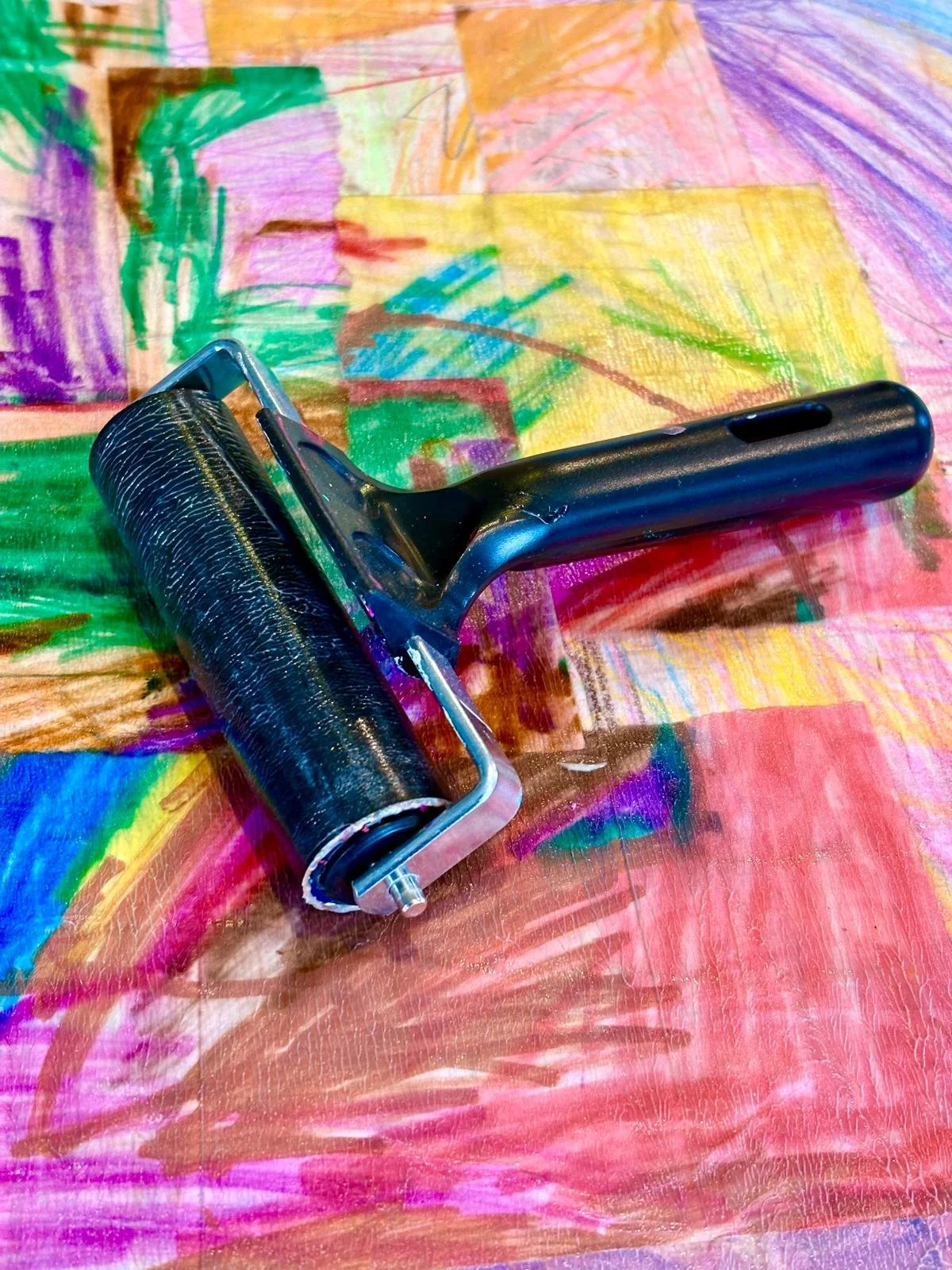 A paint roller with a black handle and a textured black roller resting on a colorful, abstract painted surface.
