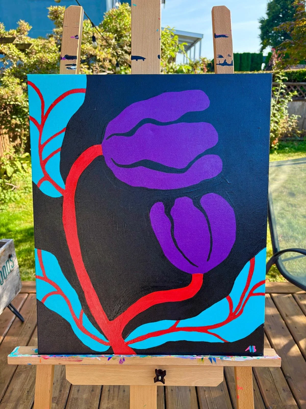 Abstract painting of a rose with purple petals, a blue background, and red vines, displayed on an easel outdoors with greenery and a blue sky in the background.