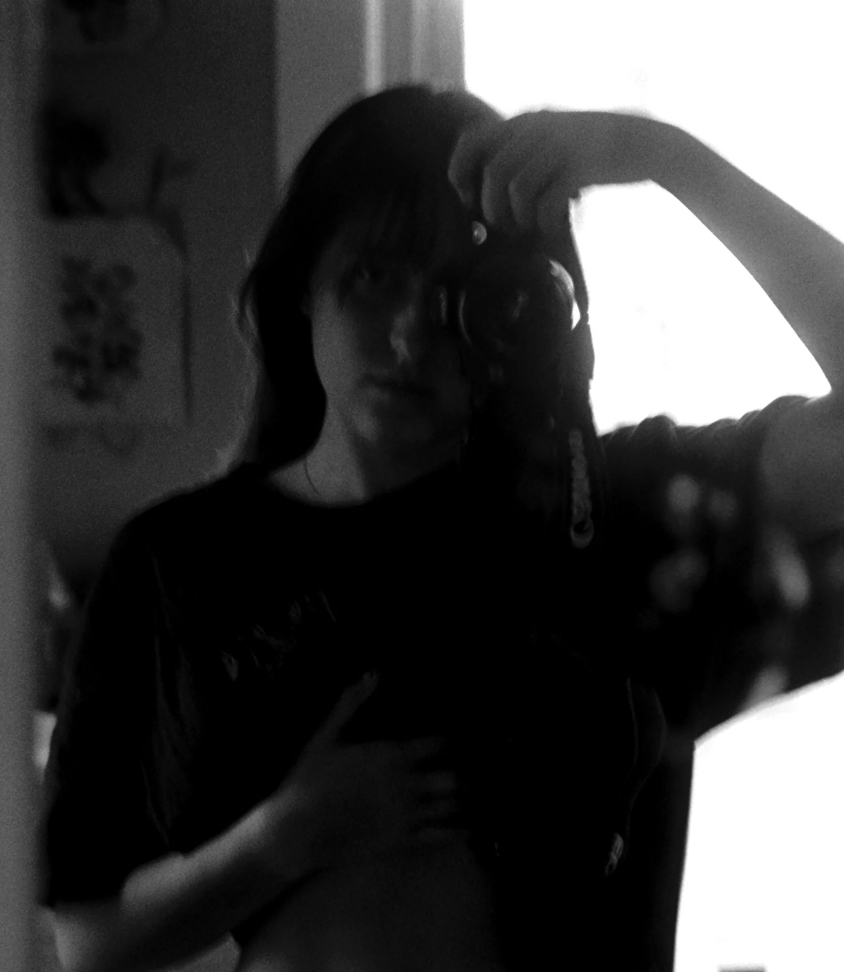 A woman taking a mirror selfie in black and white, holding a film camera.