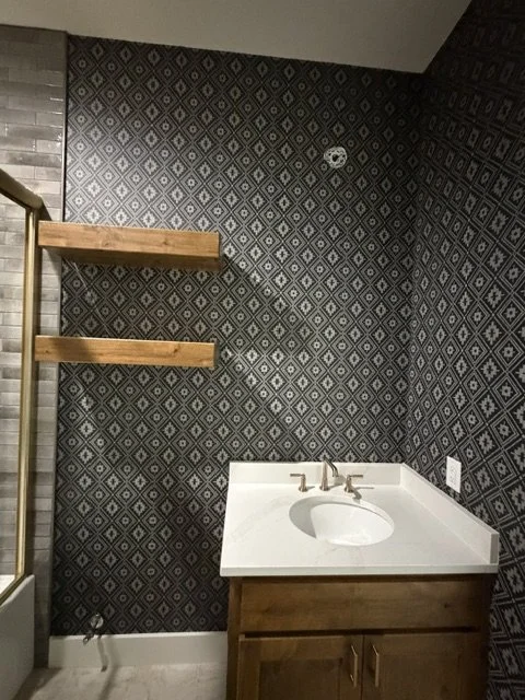 Bathroom with dark patterned wallpaper, wooden shelves, white sink, and wooden cabinet.