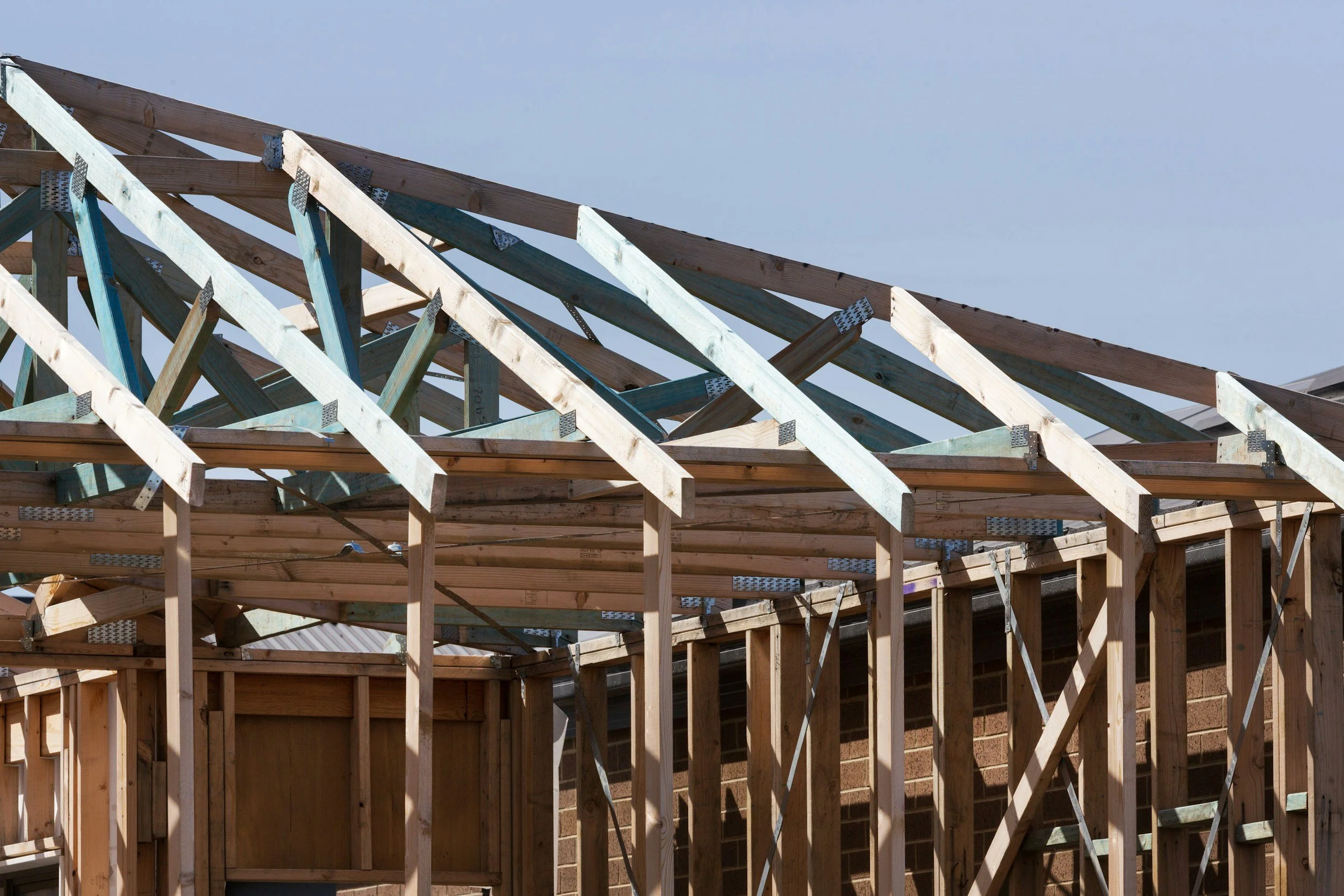Wooden framework and roof trusses under construction on a house with a blue sky background.