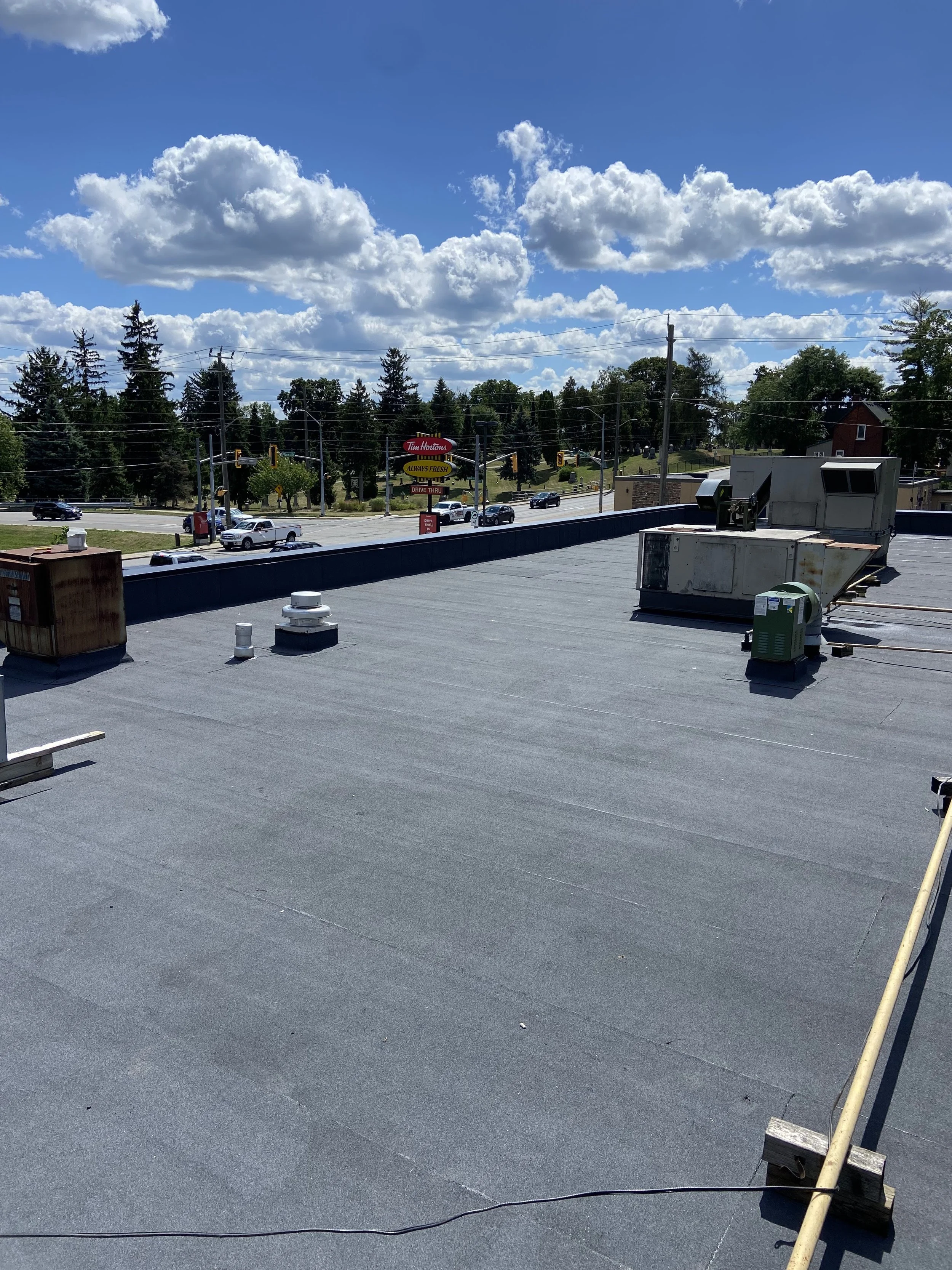 View of a parking lot rooftop under a blue sky with scattered clouds, several vents and equipment on the roof, and a street with cars and a Tim Hortons sign in the background.