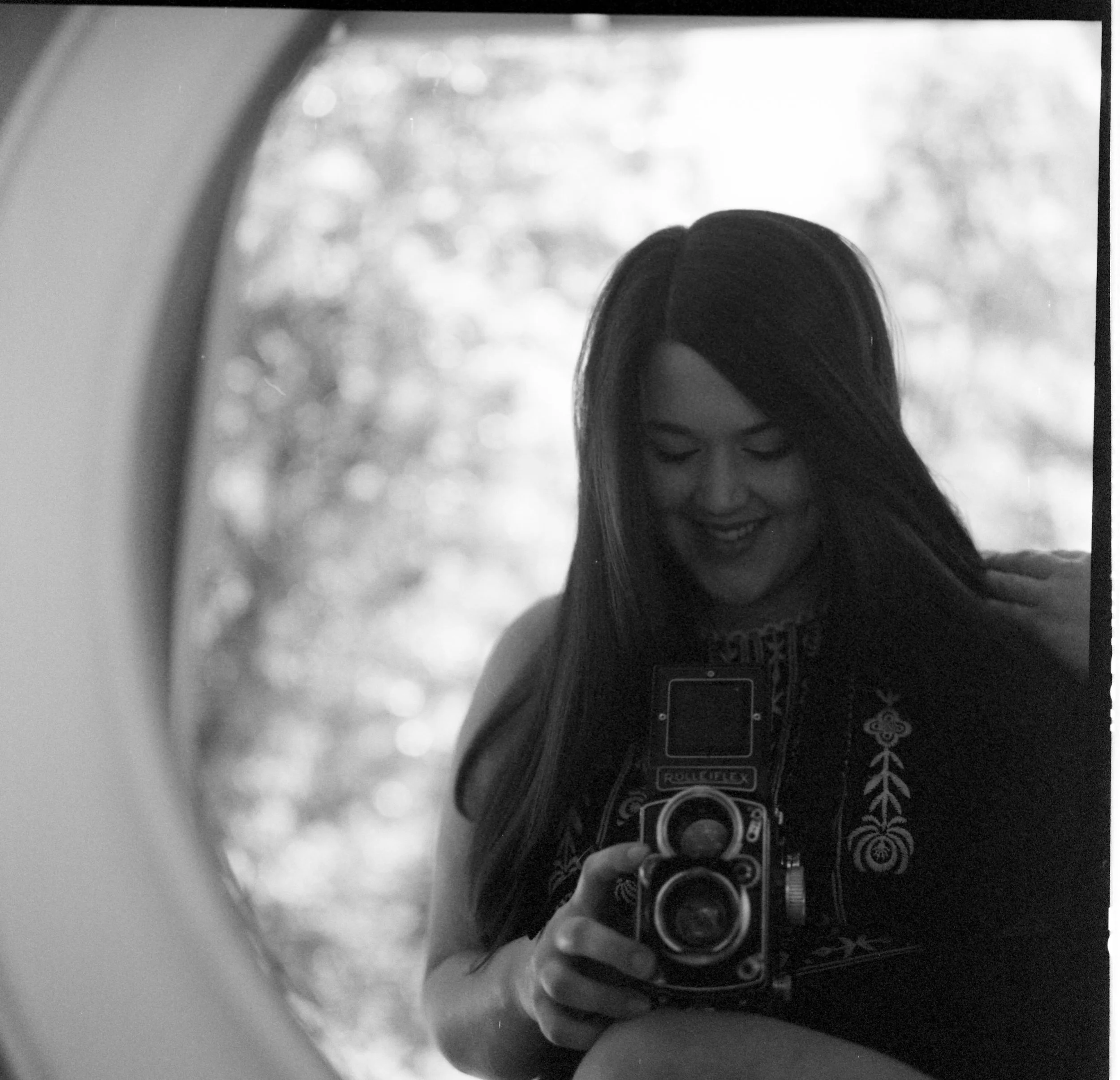 A person holding a smartphone with a black and white patterned case, taking a photo of a mirror reflection of their face and hair.