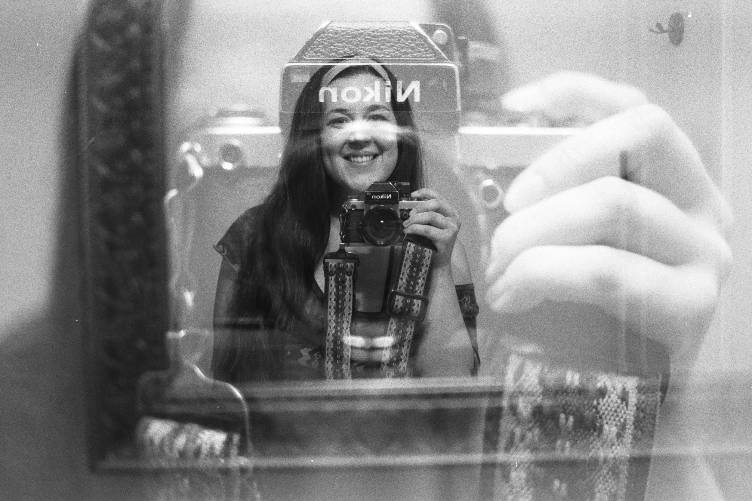 A person taking a self-portrait with a camera, reflected in a mirror with a smile, in a grayscale photo.