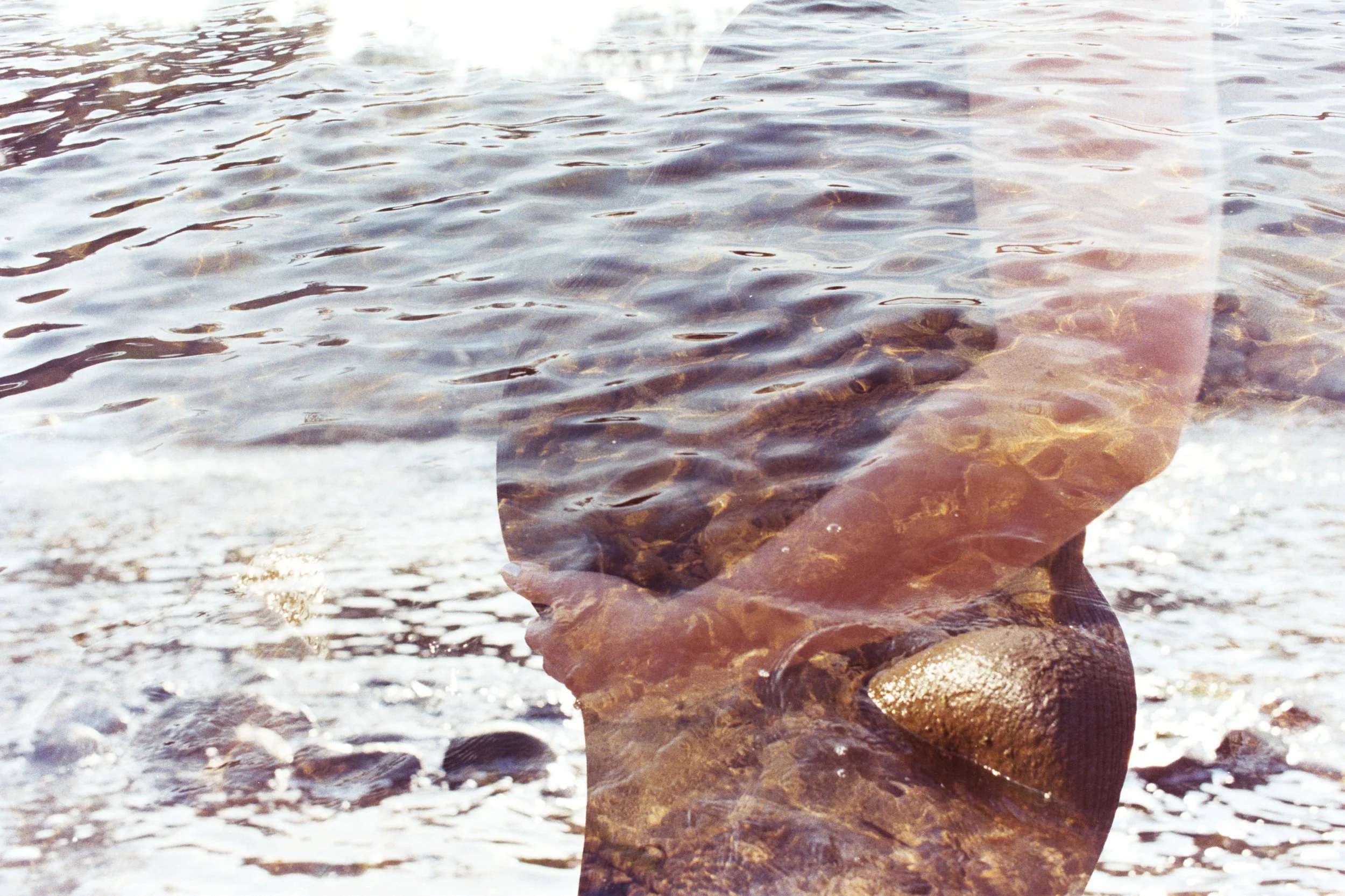 A rocky shoreline in front of a body of water, with the photo taken through a semi-transparent glass or plastic sheet.