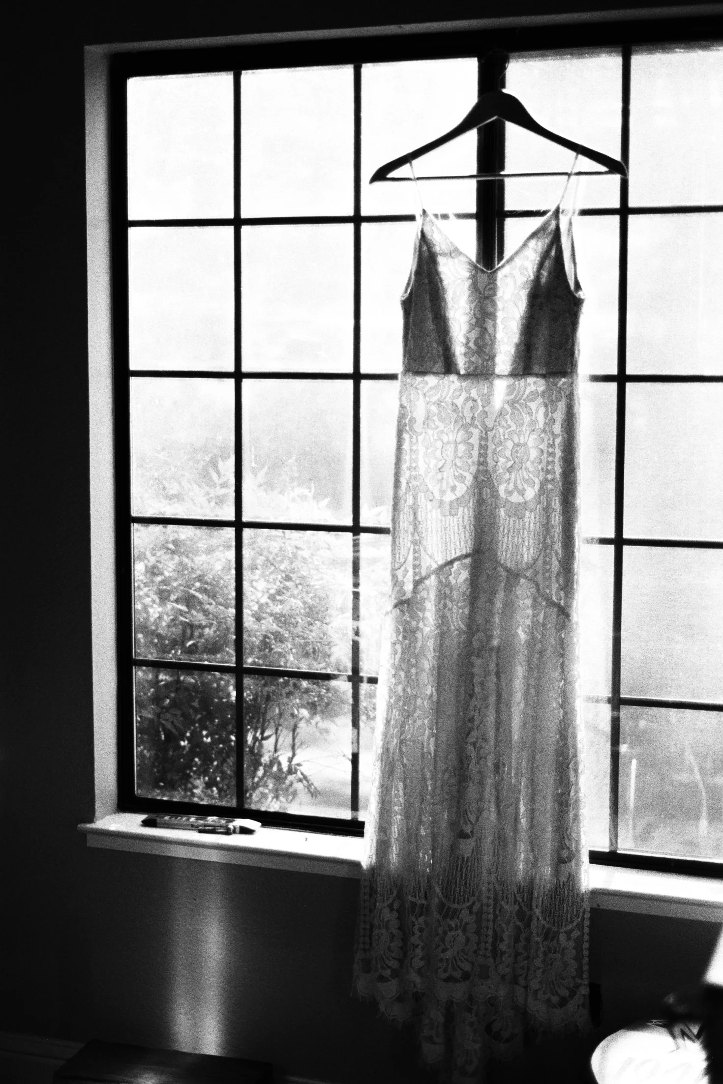 A lace dress hanging on a hanger in front of a window, with a view of trees outside.