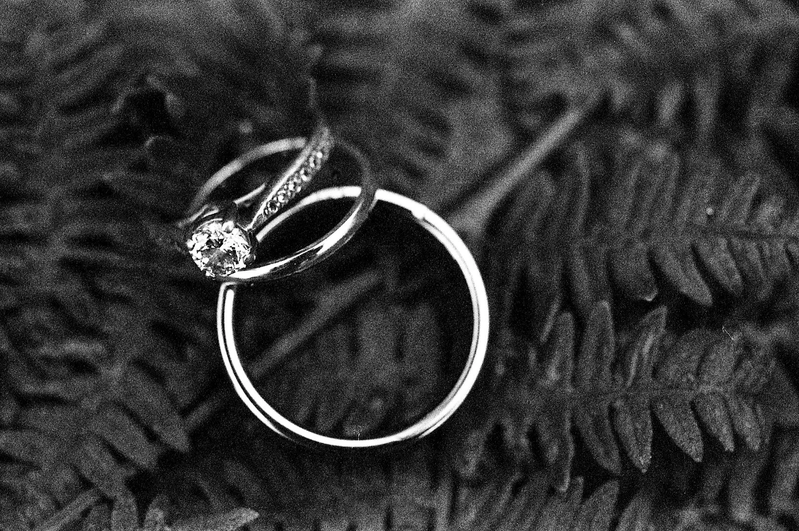 Close-up of a diamond engagement ring and wedding band on a textured black surface.
