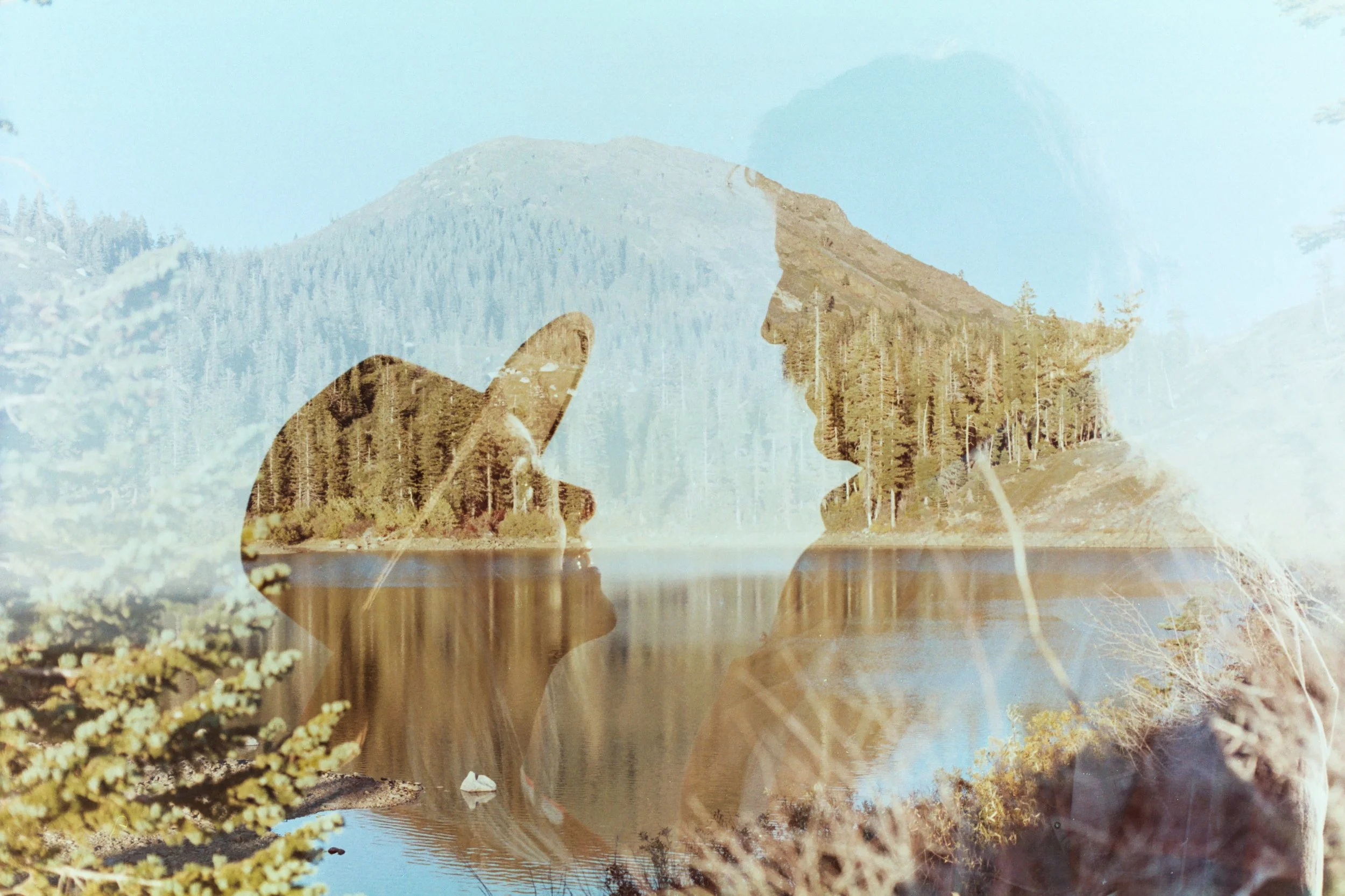 A double exposure photograph showing a close-up of a man and a woman facing each other and a landscape of a mountain, trees, and a body of water.