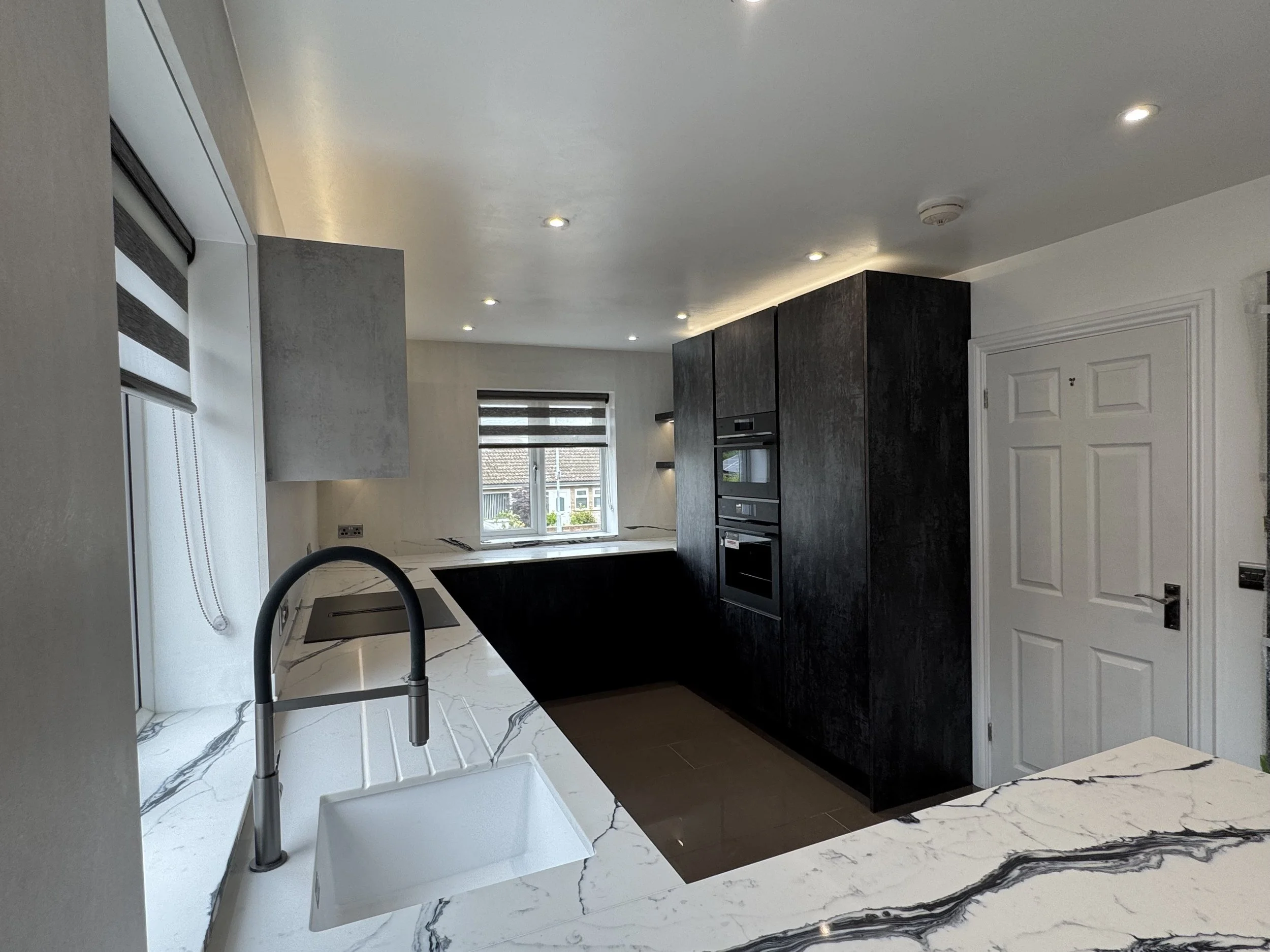 A modern kitchen with white quartz worktops, a black kitchen island, and white walls