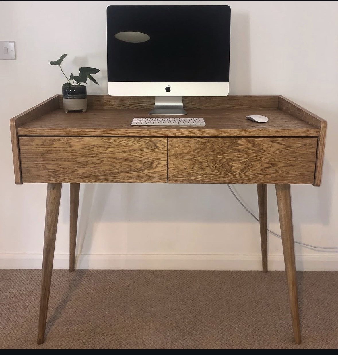 Wooden desk with an iMac computer, a wireless keyboard, and a mouse, with a small potted plant on the left side.