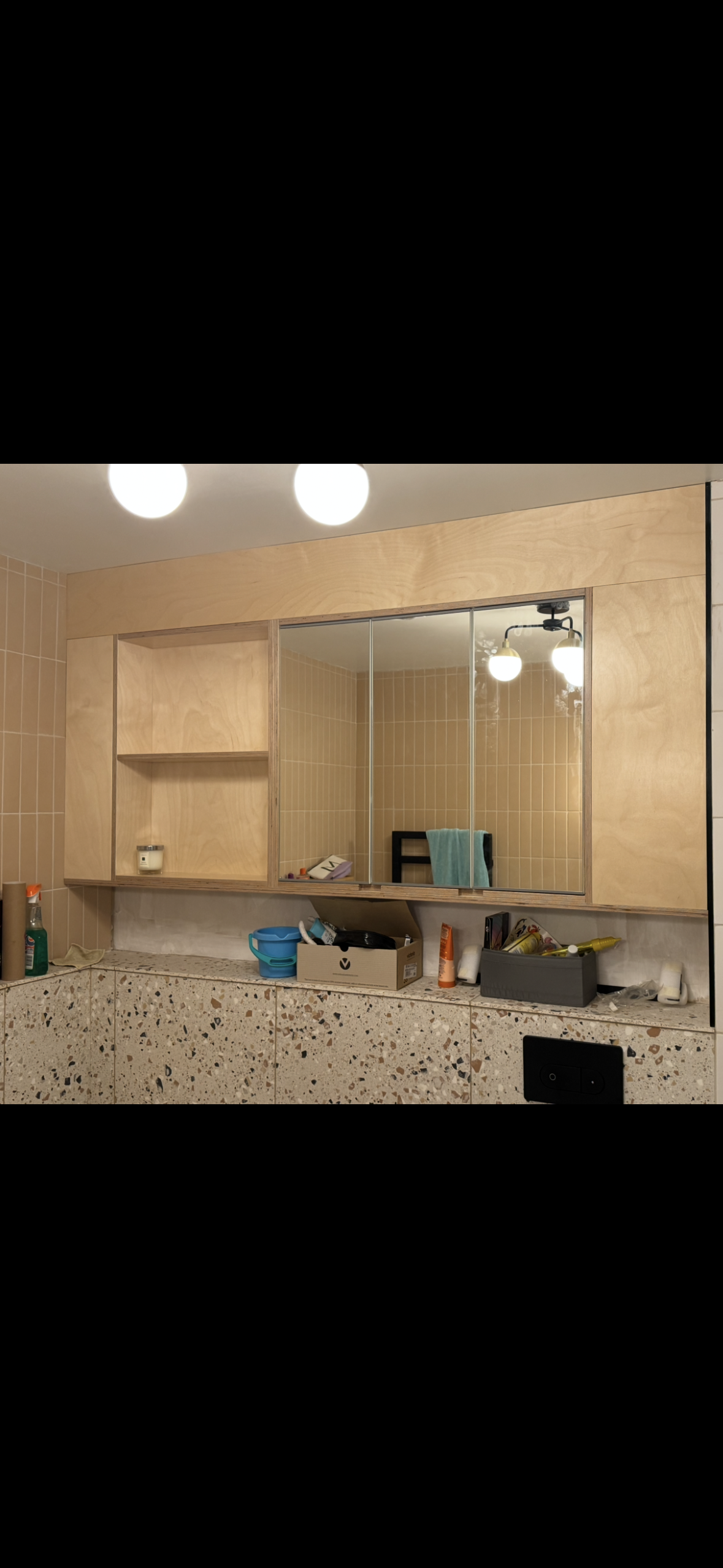 Bathroom with a large mirror, wooden cabinet, and cluttered countertop with toiletries and cleaning supplies.