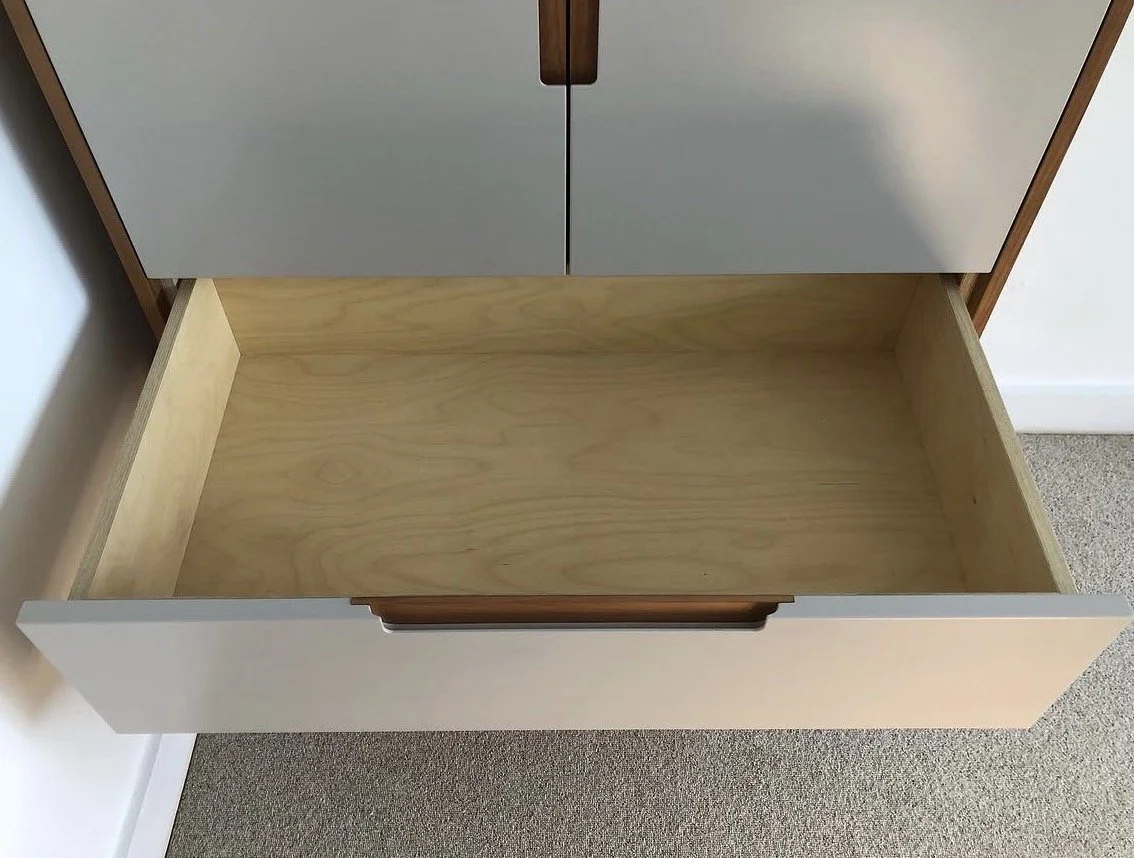 Empty drawer in a cabinet with wooden interior and white front panel.