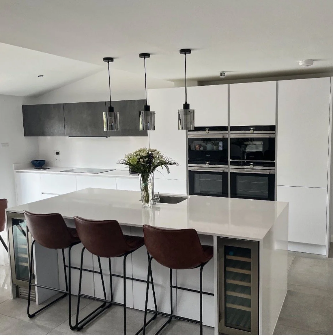 Modern kitchen with white island, brown bar stools, black pendant lights, and built-in black appliances