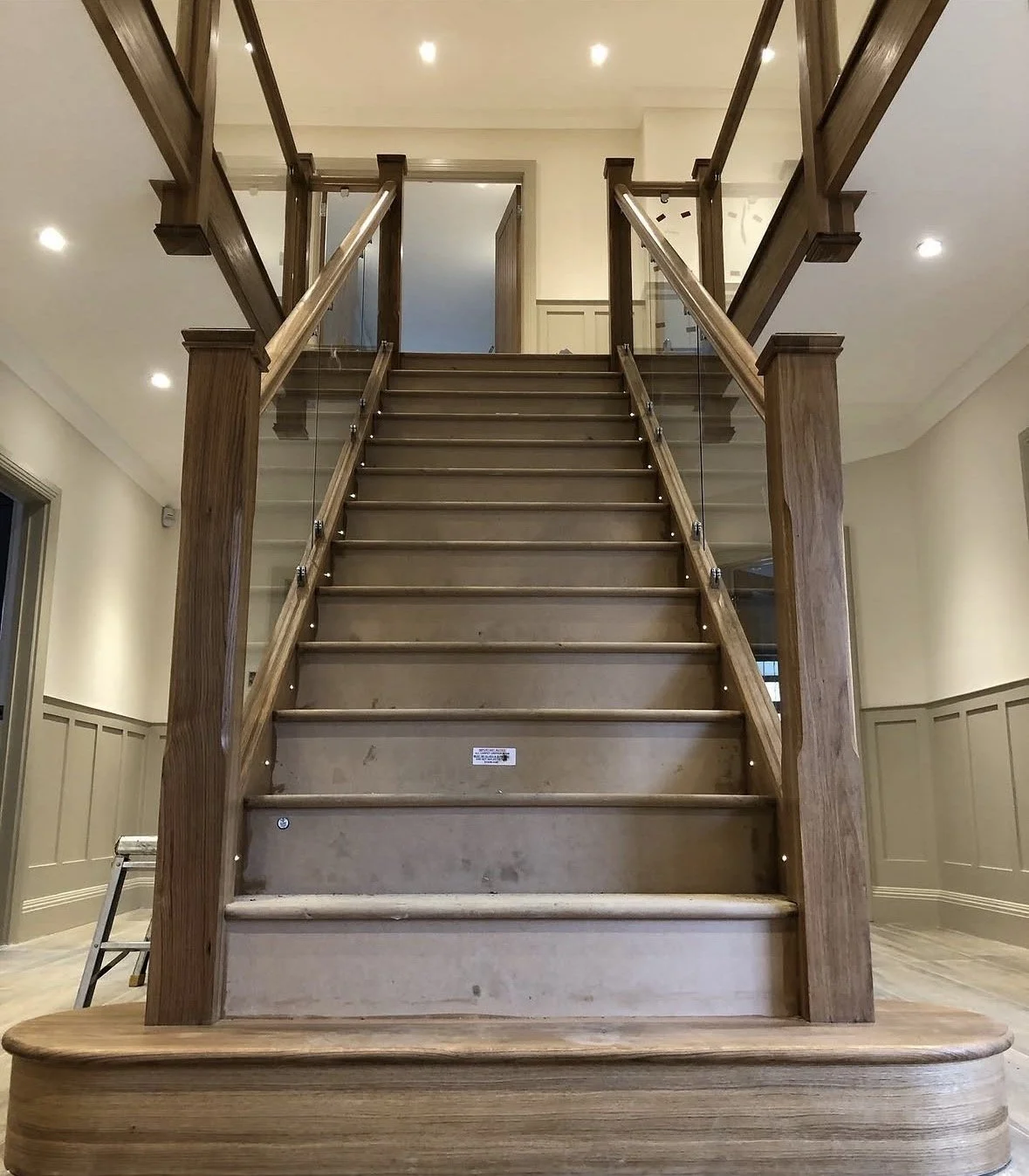 Wood staircase with glass railing in a well-lit interior space.