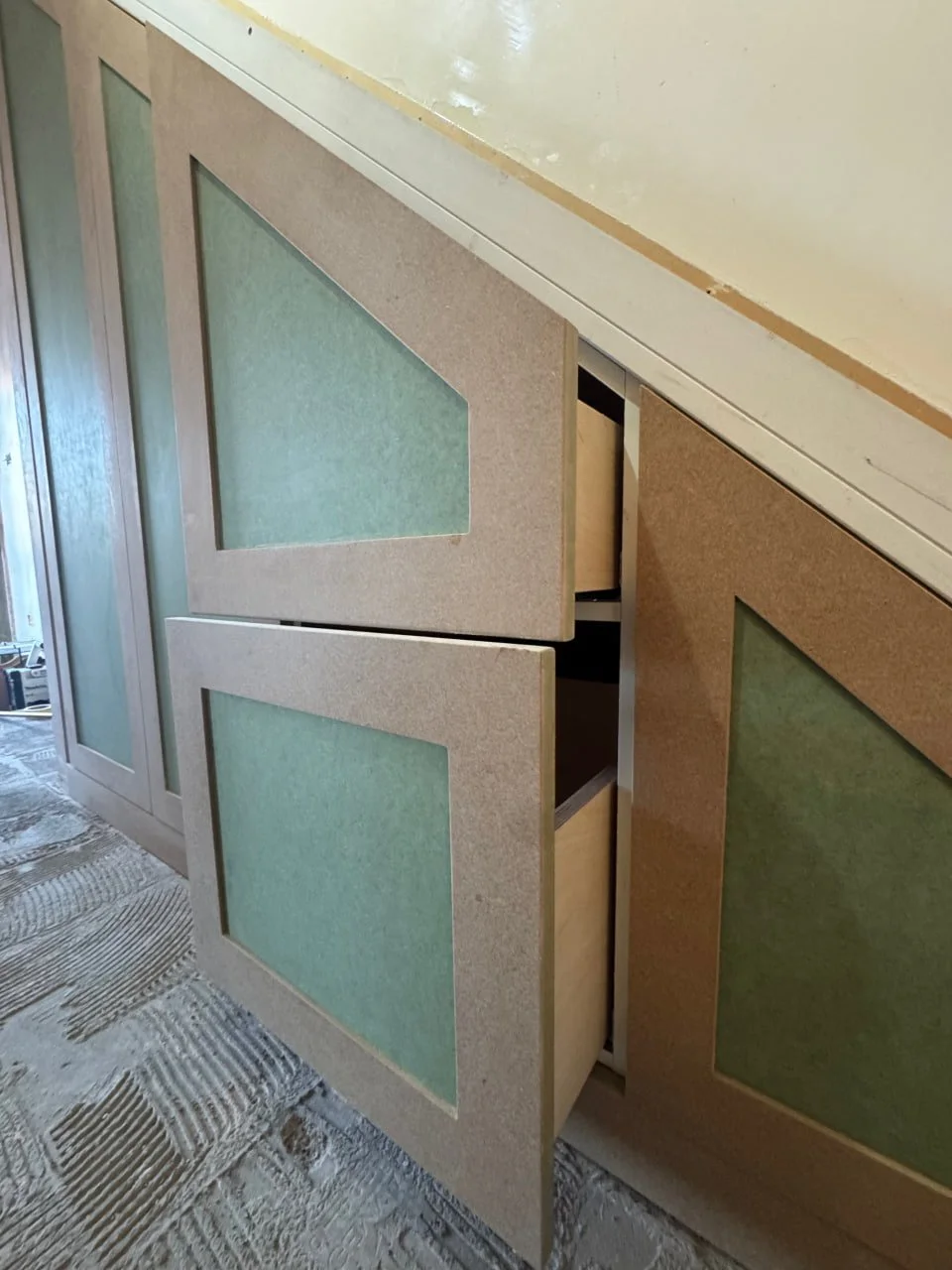 Close-up of a partially open wooden cabinet with light-colored panels and frosted glass inserts, revealing empty shelves inside, with a textured carpeted floor in the foreground.