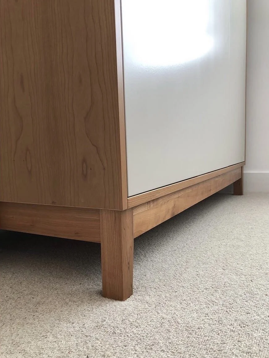 Close-up of a wooden cabinet leg and corner with a beige carpeted floor.