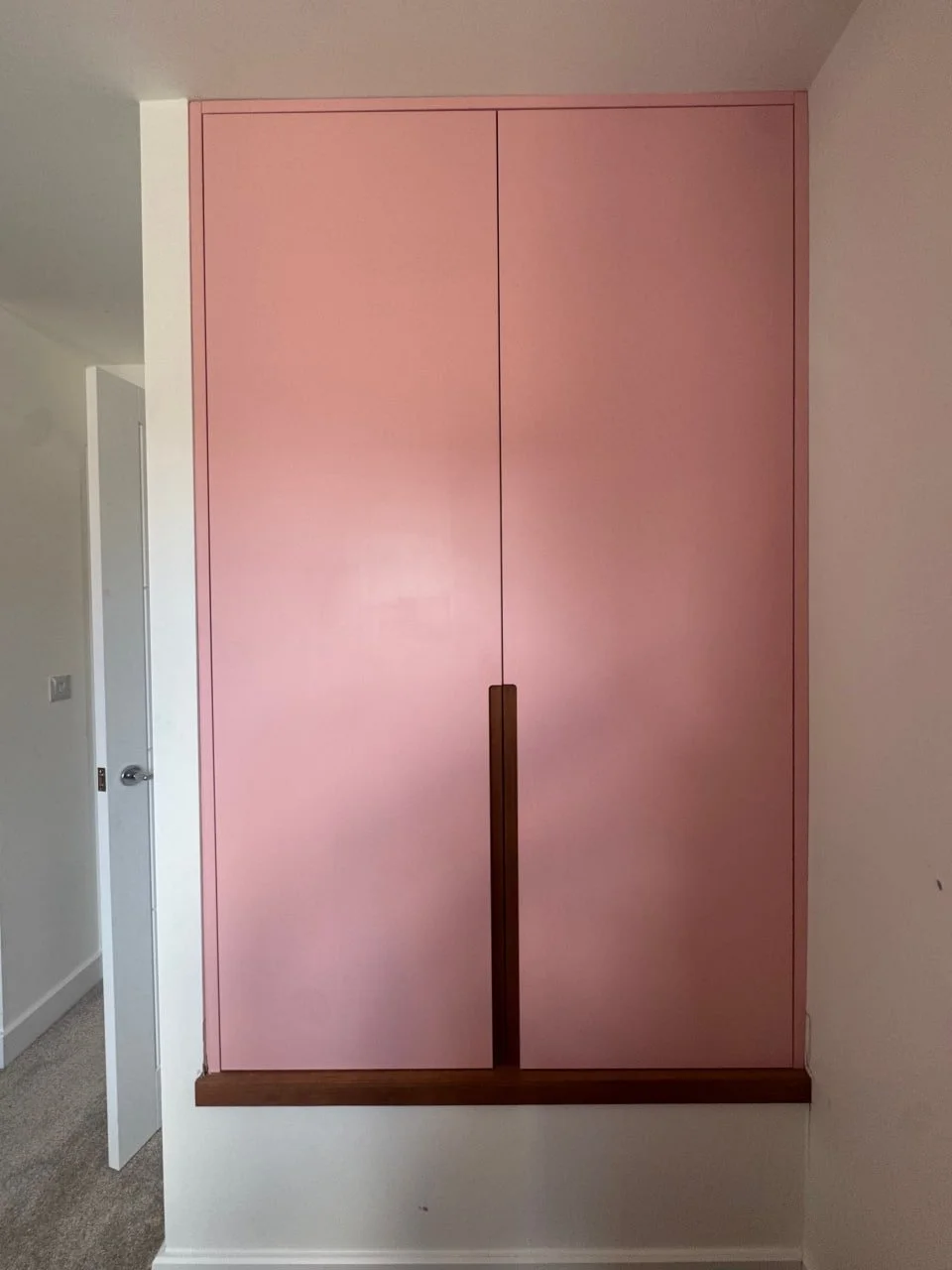 Pink closet doors with a dark brown handle and trim, located in a white wall interior.