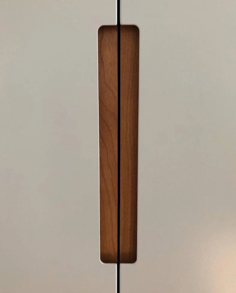 Close-up of a light-colored cabinet door with a vertical wooden handle in the center.