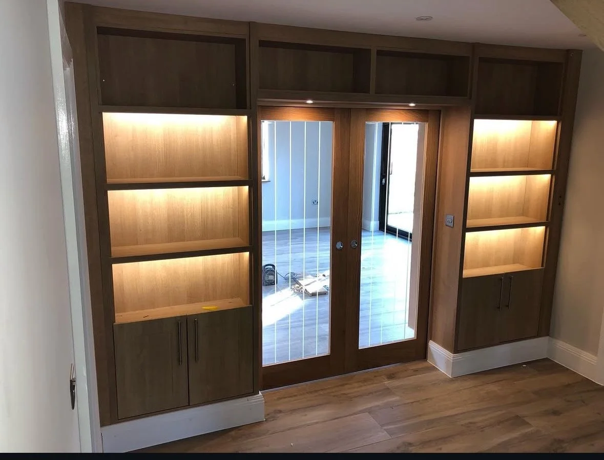 Built-in wooden shelves and cabinets surrounding glass double doors leading to an outdoor area with wooden flooring.