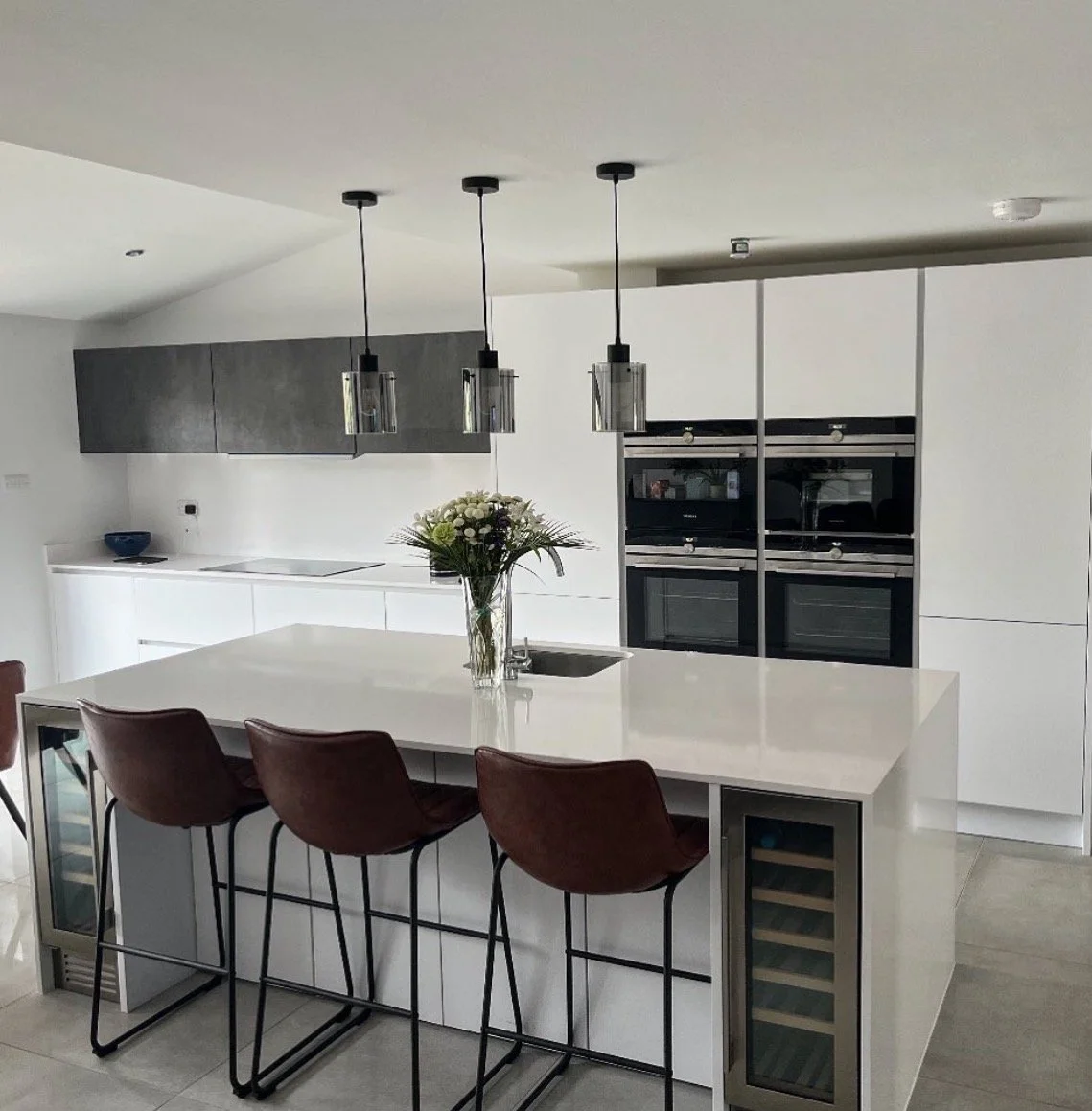 Modern kitchen with white island counter, brown barstools, black pendant lights, black and white cabinetry