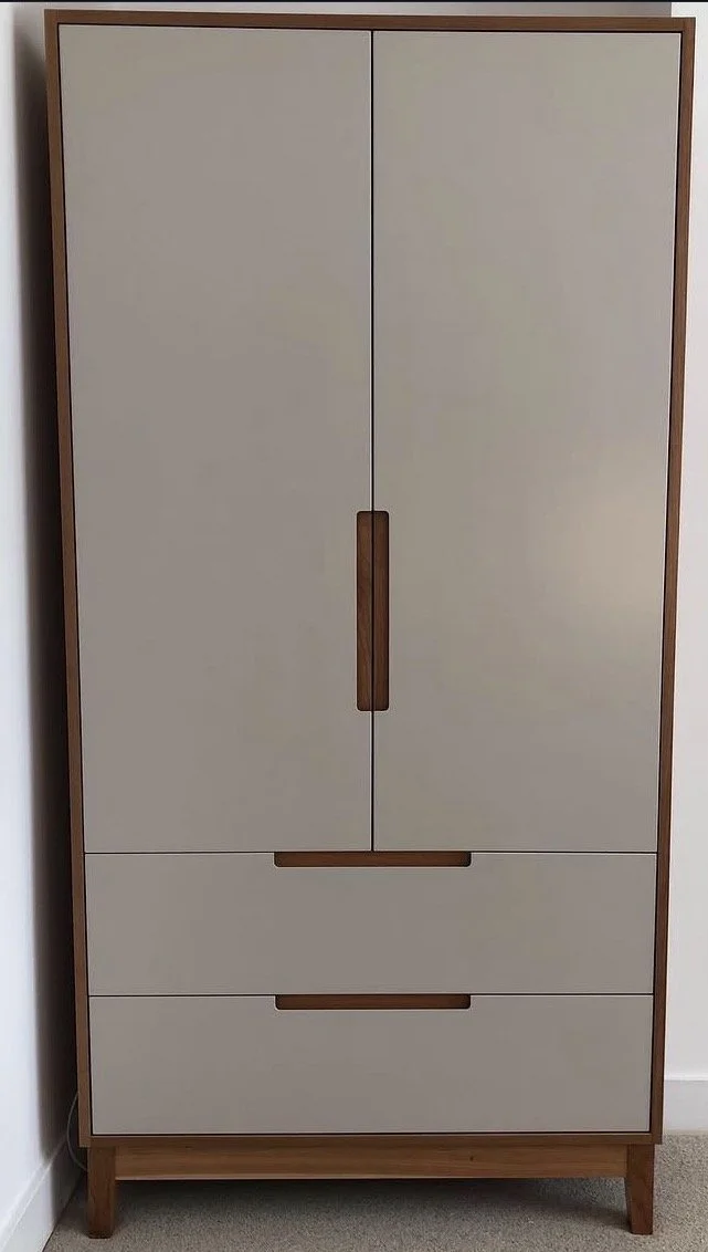A modern wardrobe with two large upper doors and two lower drawers, featuring wooden handles and trim, standing on wooden legs.