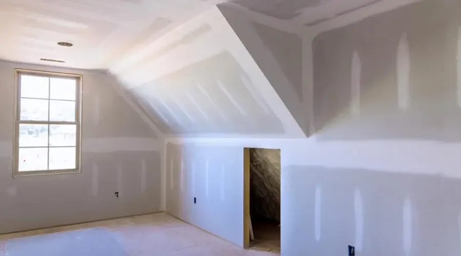 An unfinished attic room with drywall installed on the walls and ceiling, a window letting in natural light, and a small door opening to a storage space or crawl area in St George UT
