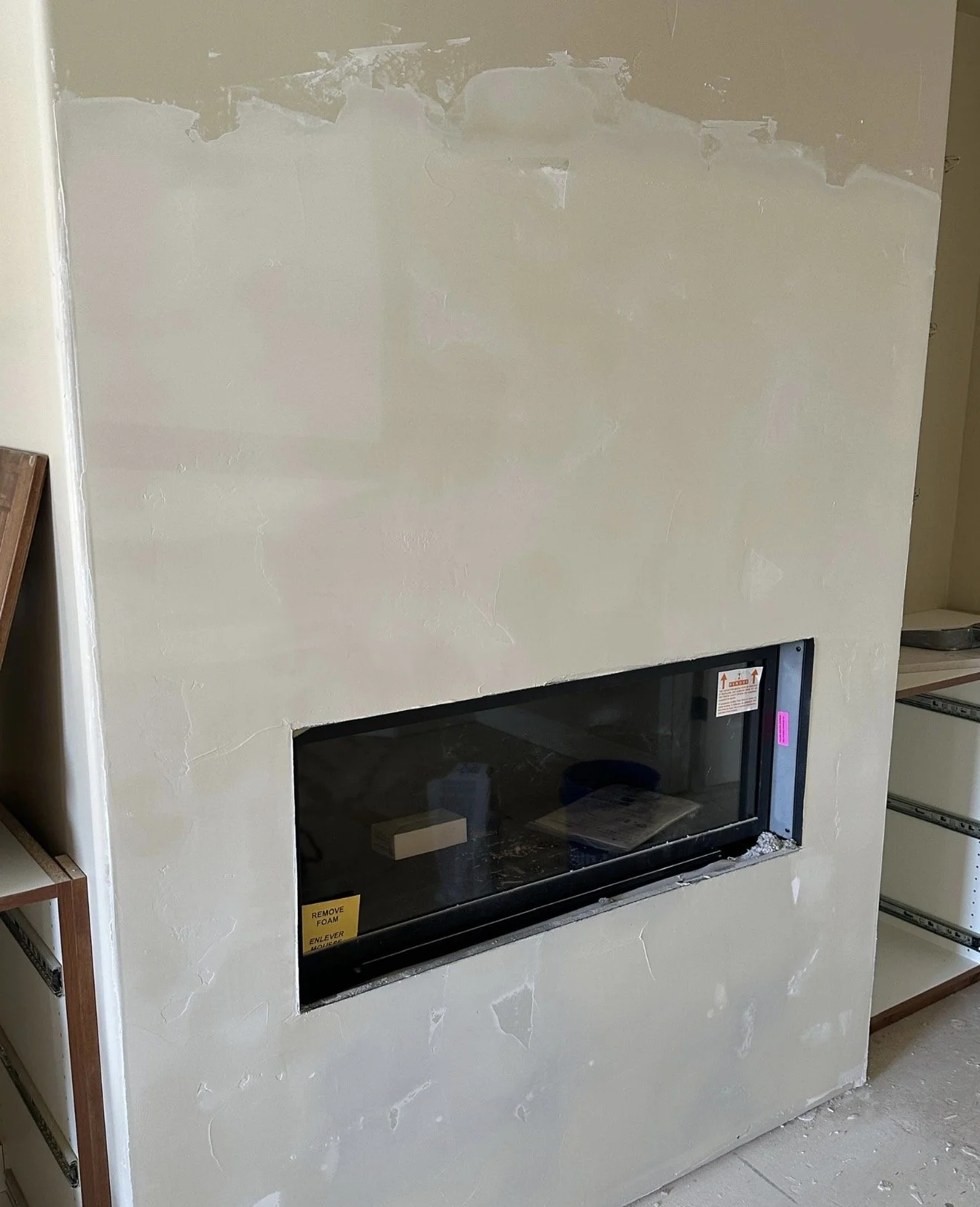 Image of a partially finished wall with a built-in fireplace opening, surrounded by unpainted drywall and construction materials around.