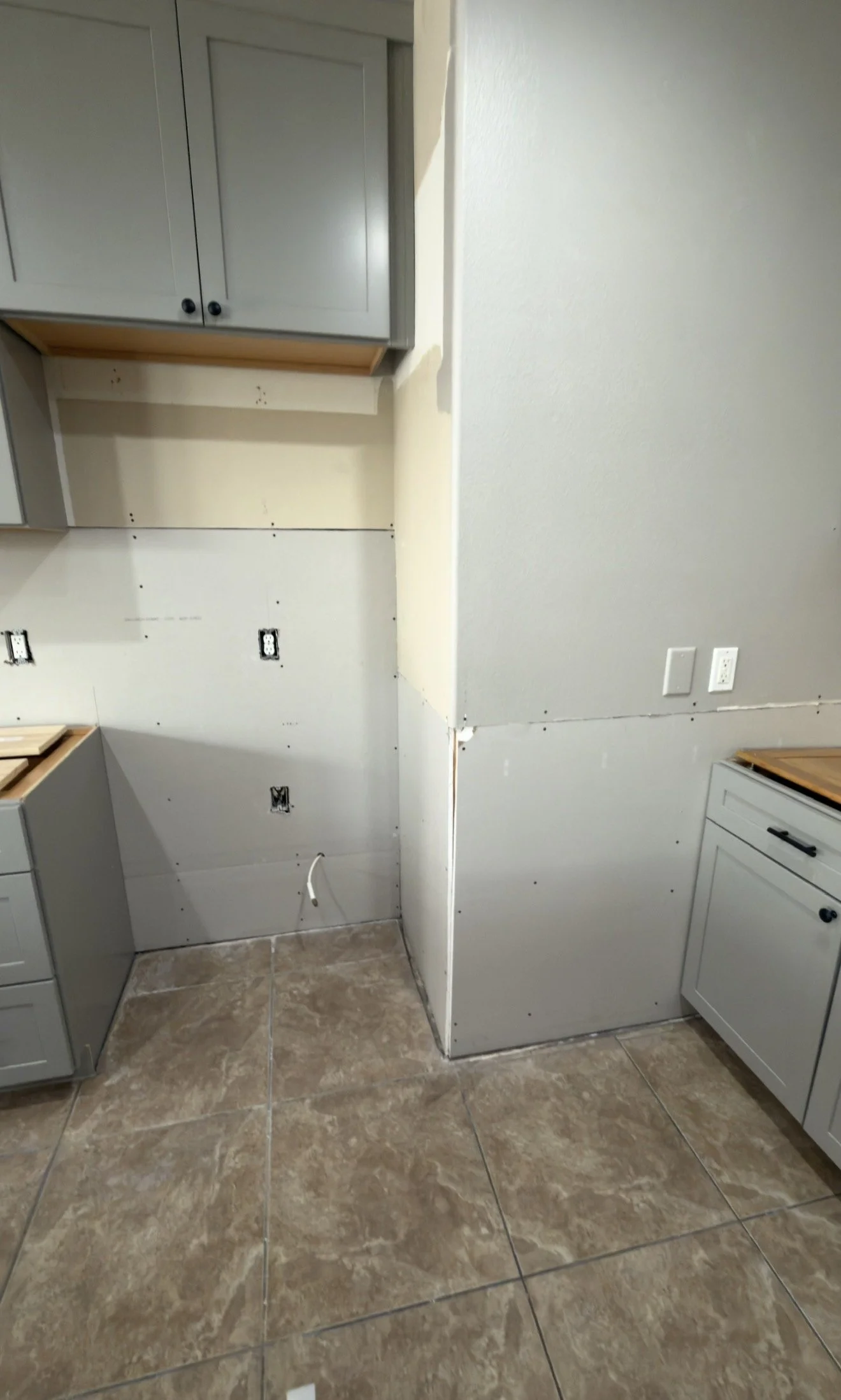 Kitchen under renovation with unfinished cabinets, exposed walls, and electrical outlets, and tiled flooring.