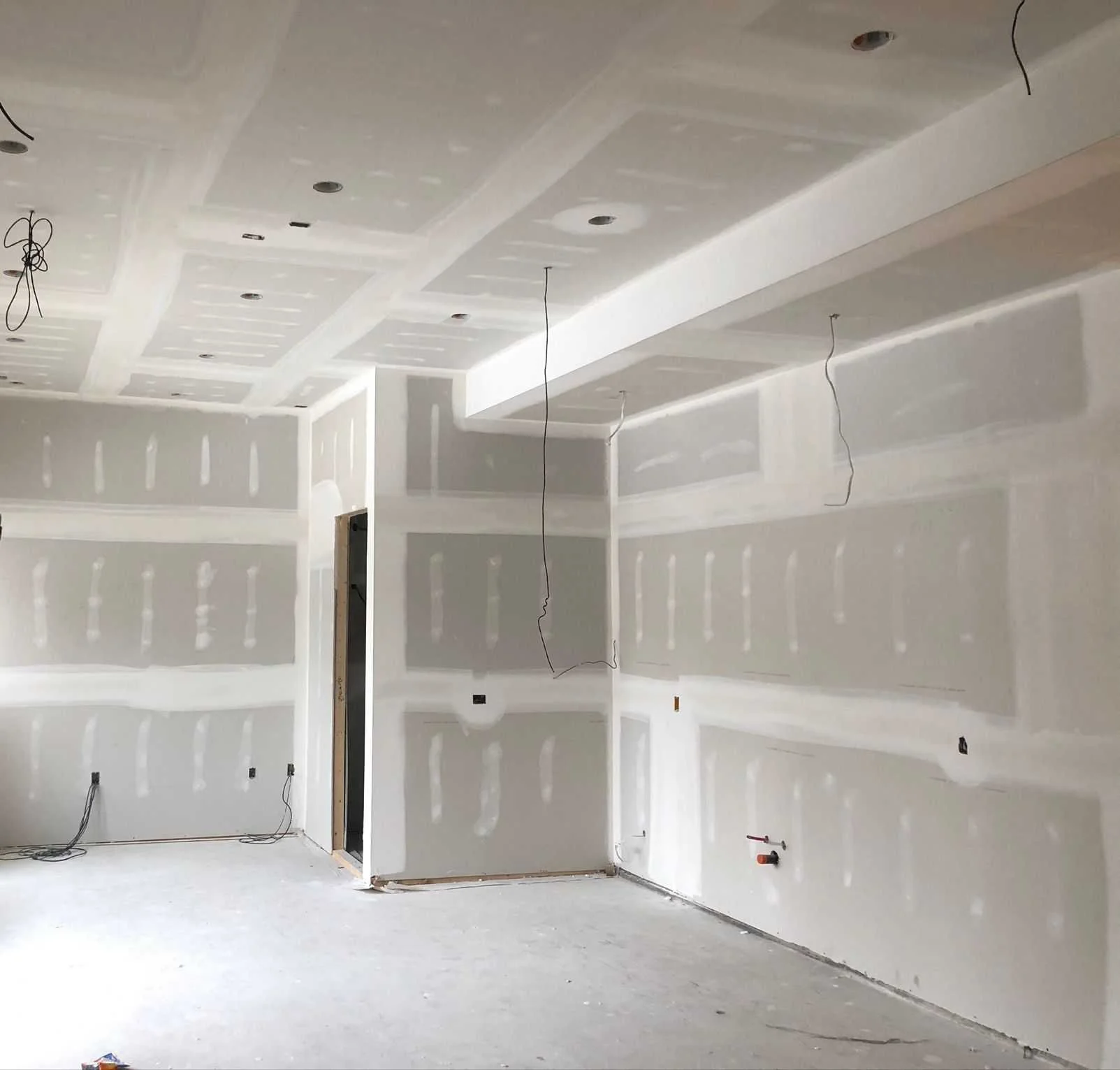 Interior of a room under construction with drywall walls and ceiling, exposed wiring, and no finished flooring.