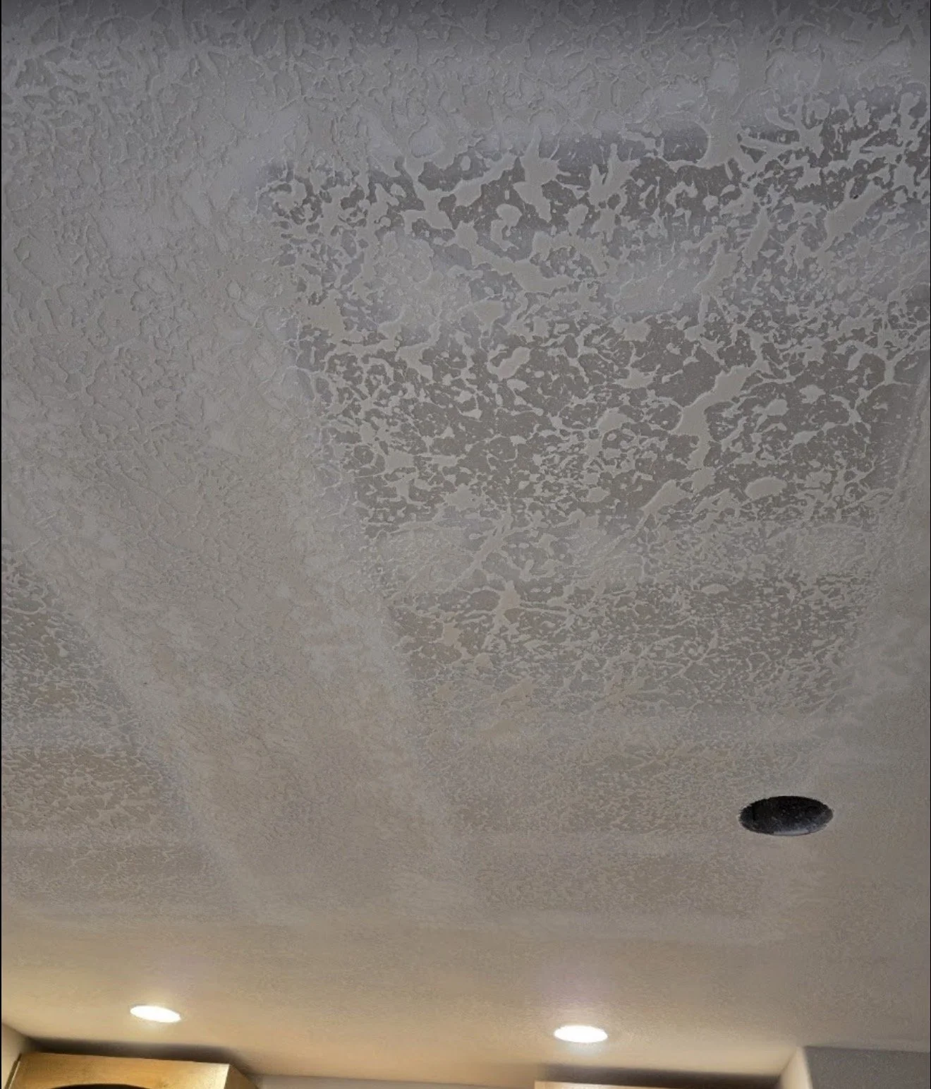 Ceiling with textured paint and recessed lighting, with a small round hole.