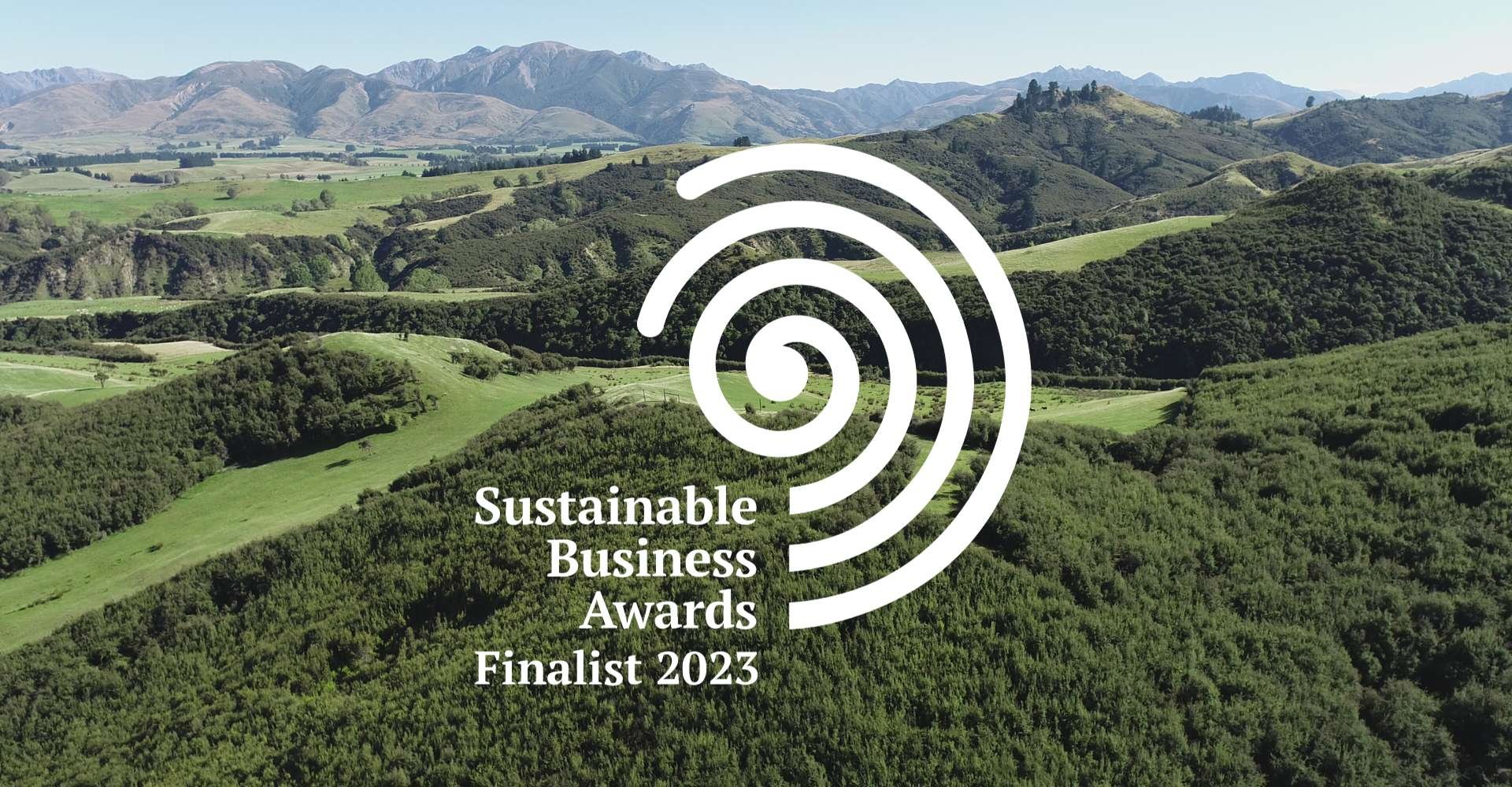 A forest and farmland landscape with mountains in the background and the Sustainable Business Awards Finalist 2023 logo on top
