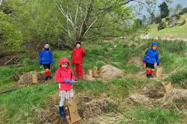 A small group of children smiling at the camera while planting trees