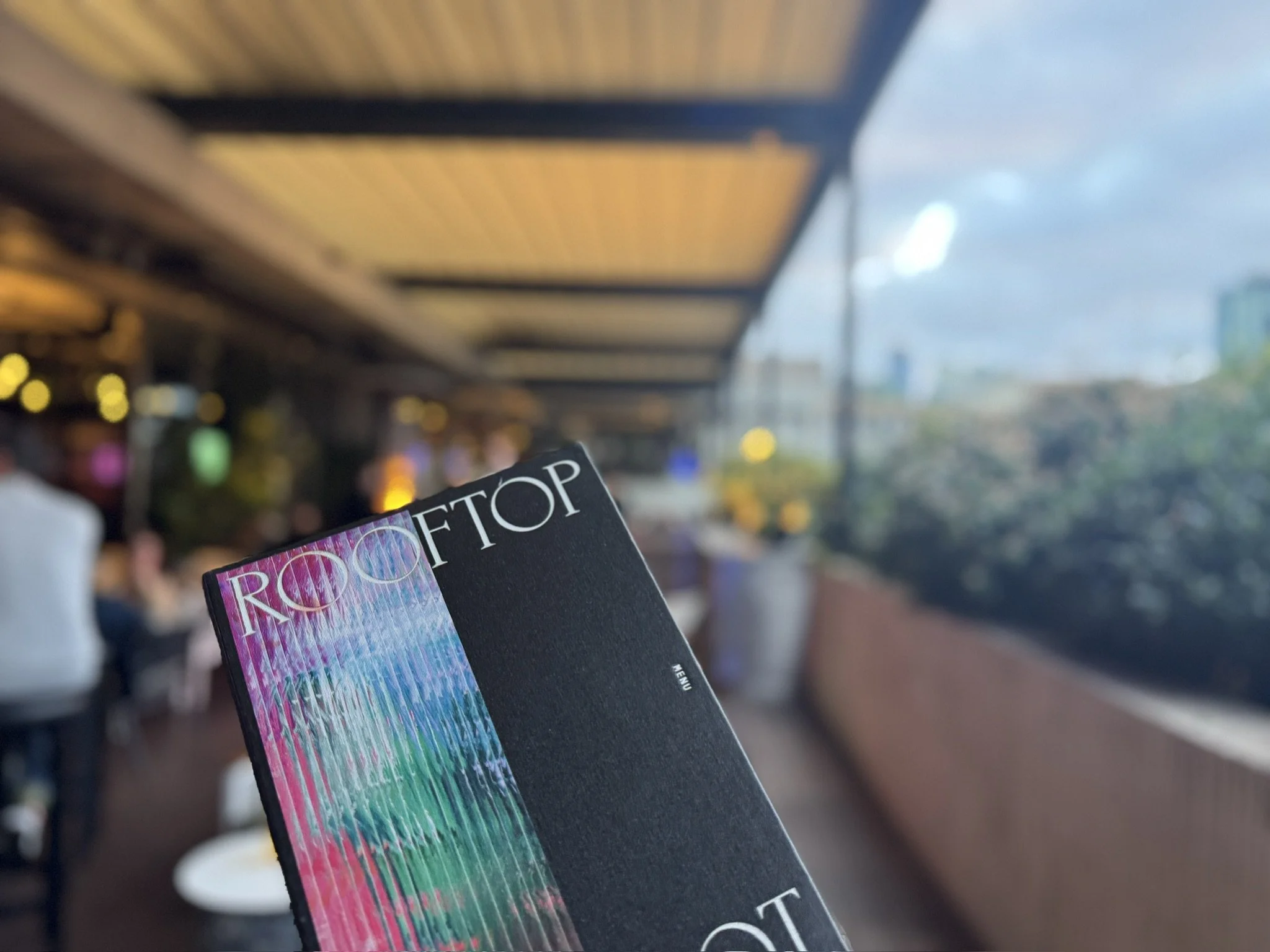 A blurred view of a city street with a table and chairs outside, and a person holding a magazine titled 'POP.' The magazine's cover features colorful, abstract artwork.