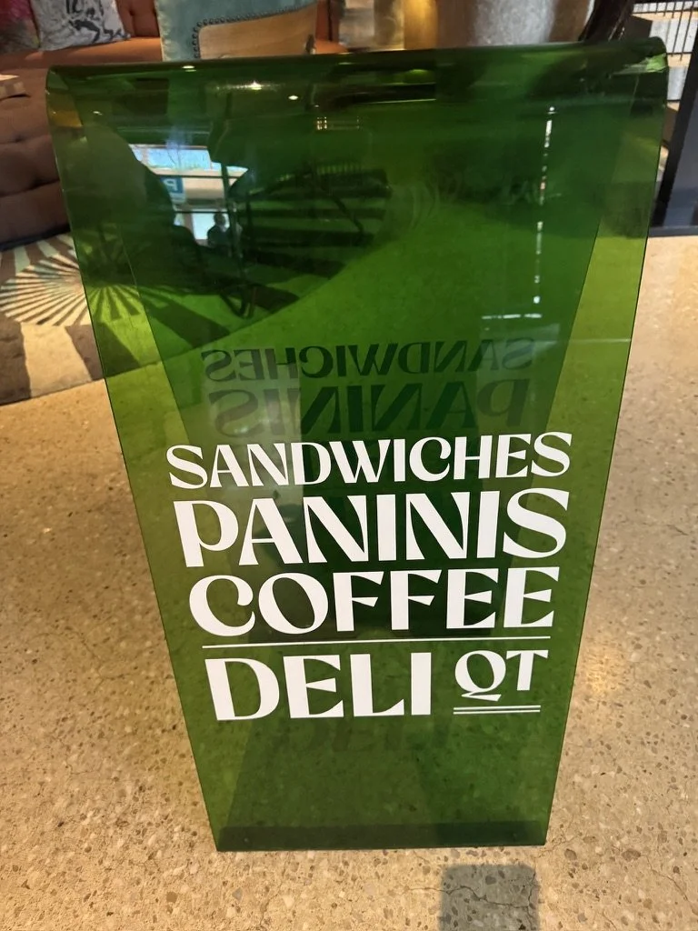 Green menu board displaying food items including sandwiches, paninis, coffee, and a deli.