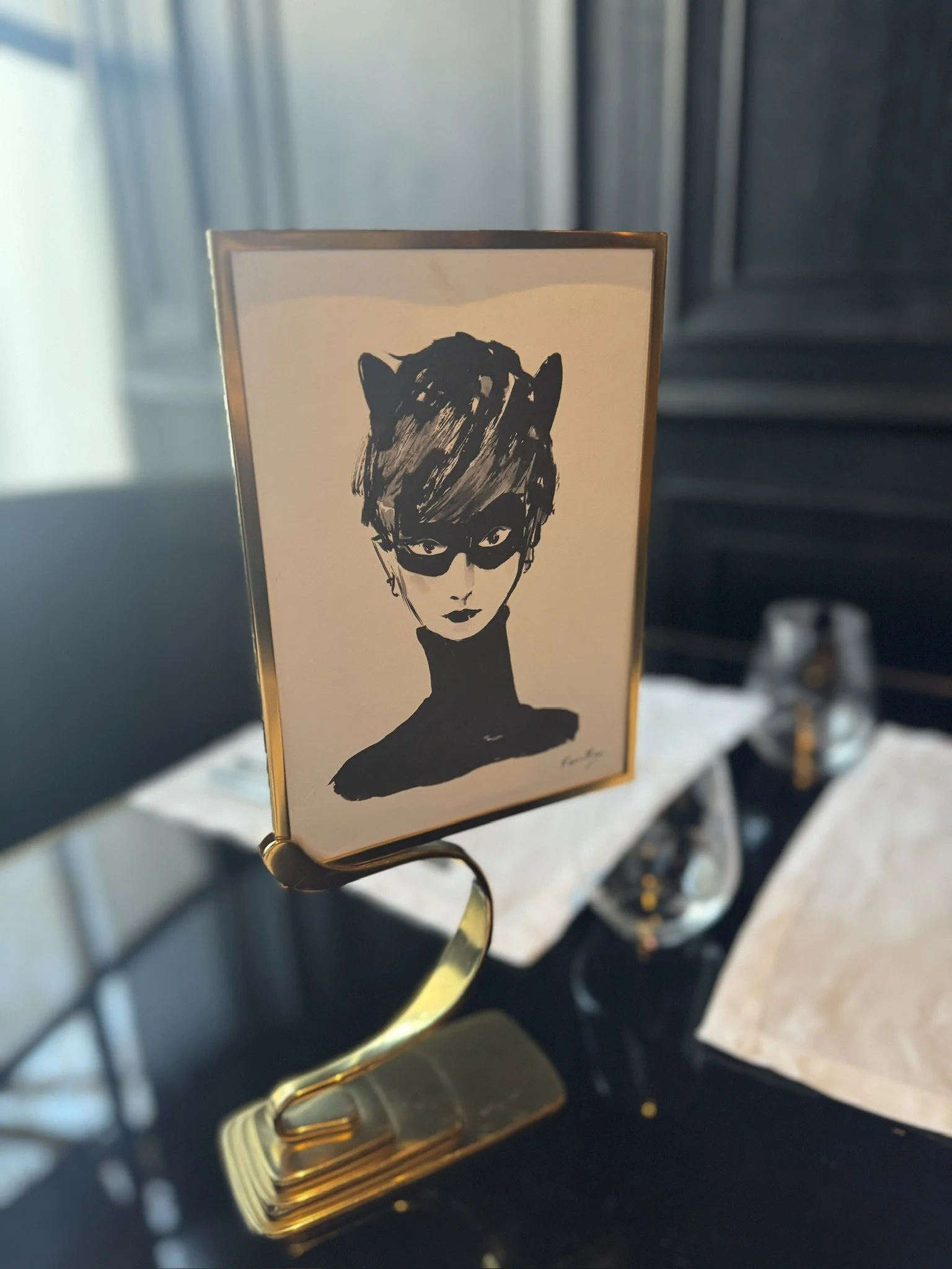 Close-up of a decorative clip holding a card with a black and white drawing of a woman with short hair and a black mask.