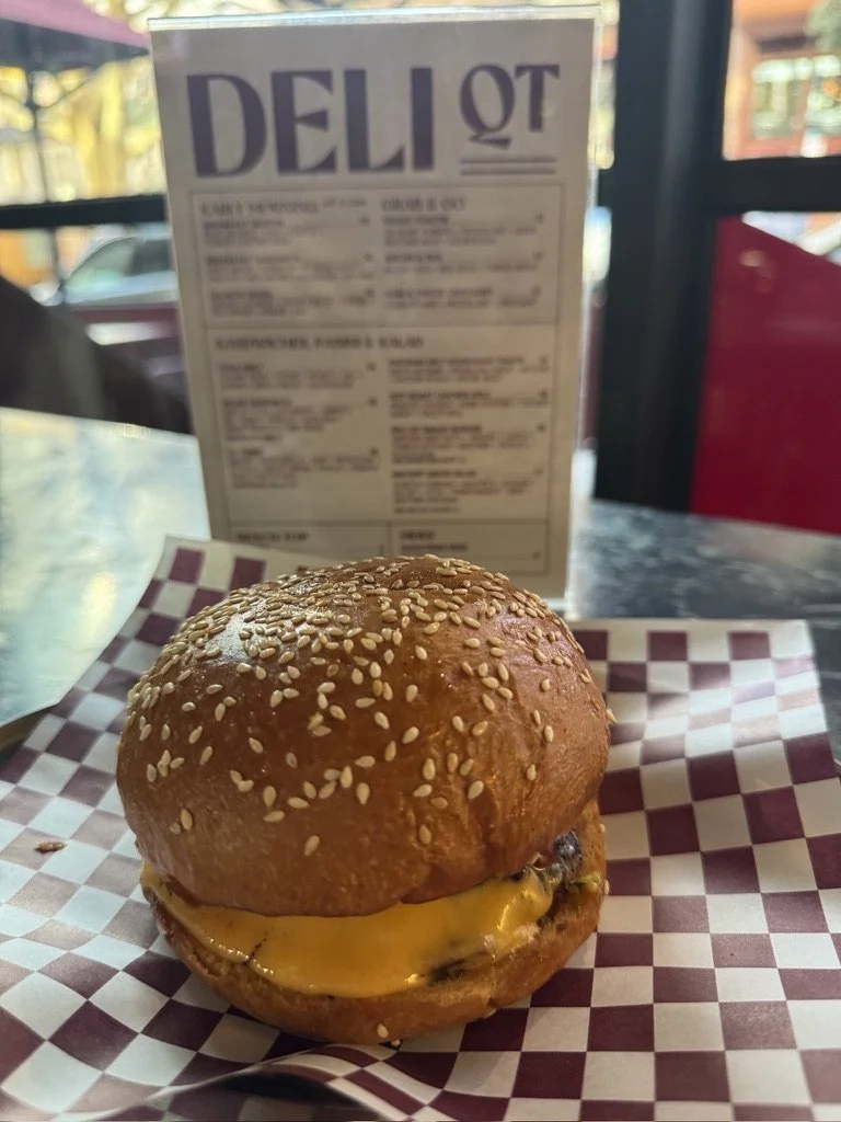 Cheeseburger with sesame seed bun on checkered restaurant tray with menu in background.