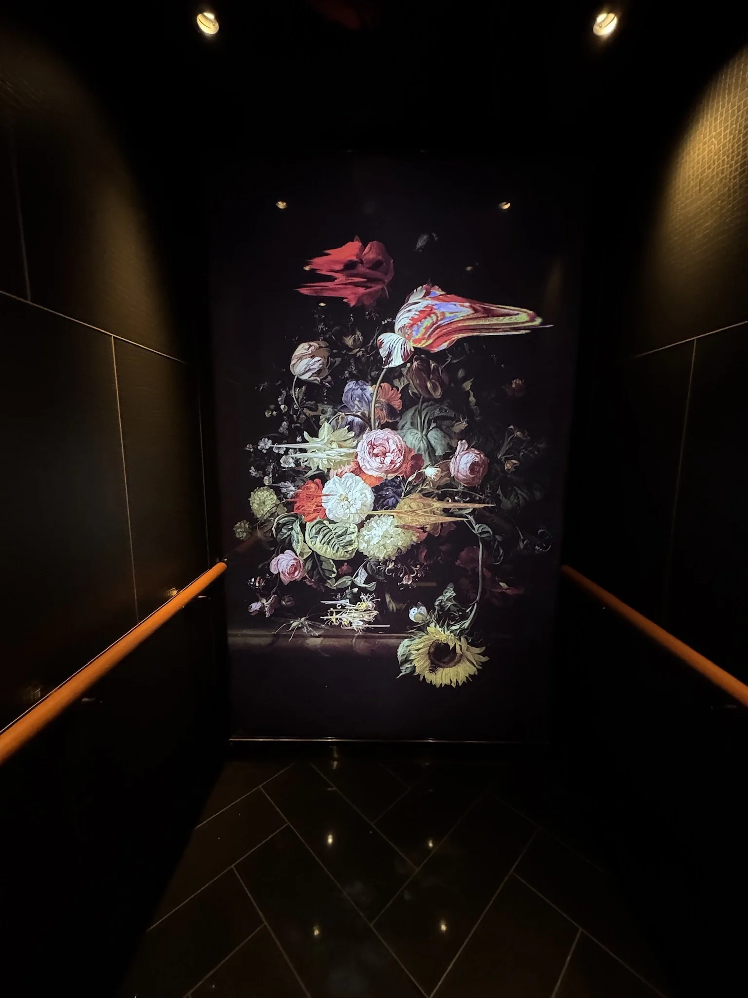 Dark hallway with a large floral painting featuring vibrant flowers and butterflies, illuminated by ceiling lights.