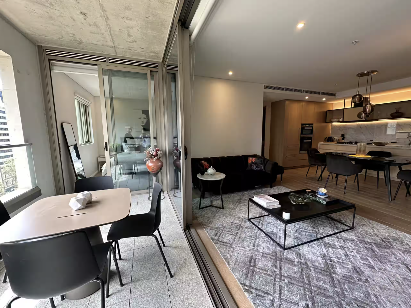 Modern open-concept living room and dining area with balcony, black sofa, coffee table, kitchen with pendant lighting, and dining table with chairs.