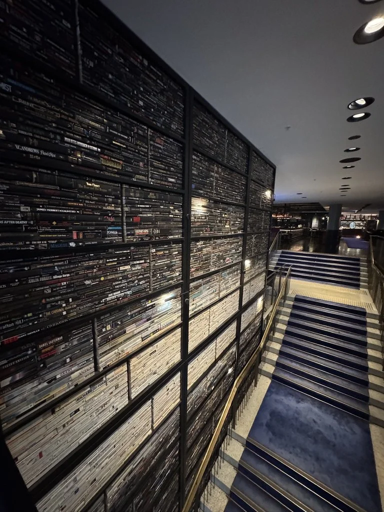Interior of a building with shelves filled with DVDs or Blu-rays on the left side and a staircase with blue runners on the right side.