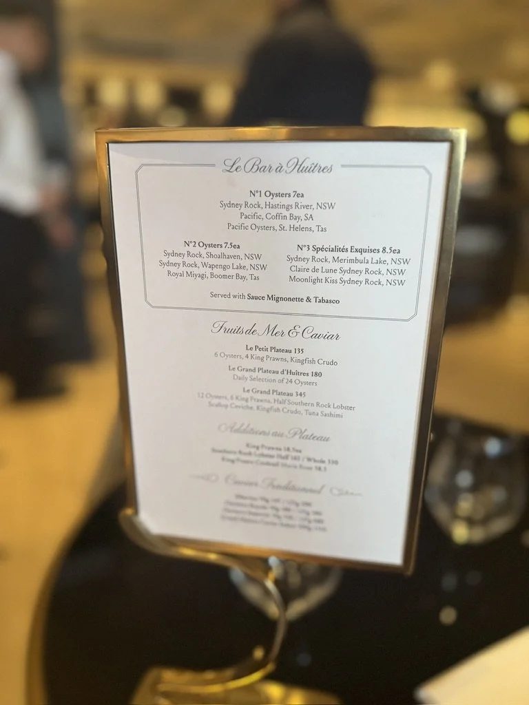 Restaurant menu featuring oysters, seafood, and caviar options, with a blurred background of a restaurant setting.