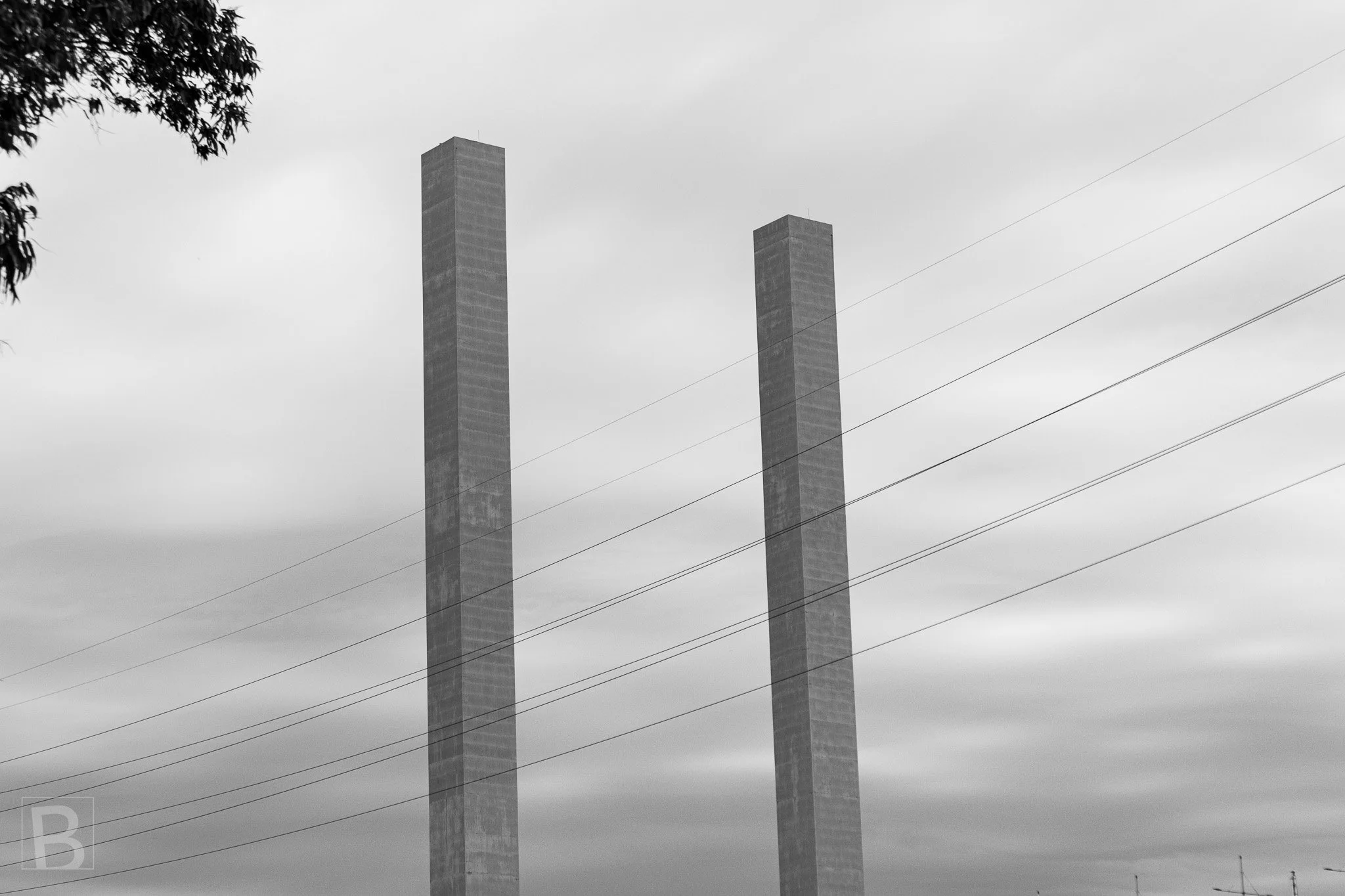 Parallel chimney stacks and fine utility lines create a quiet industrial
geometry beneath a soft, clouded sky.
