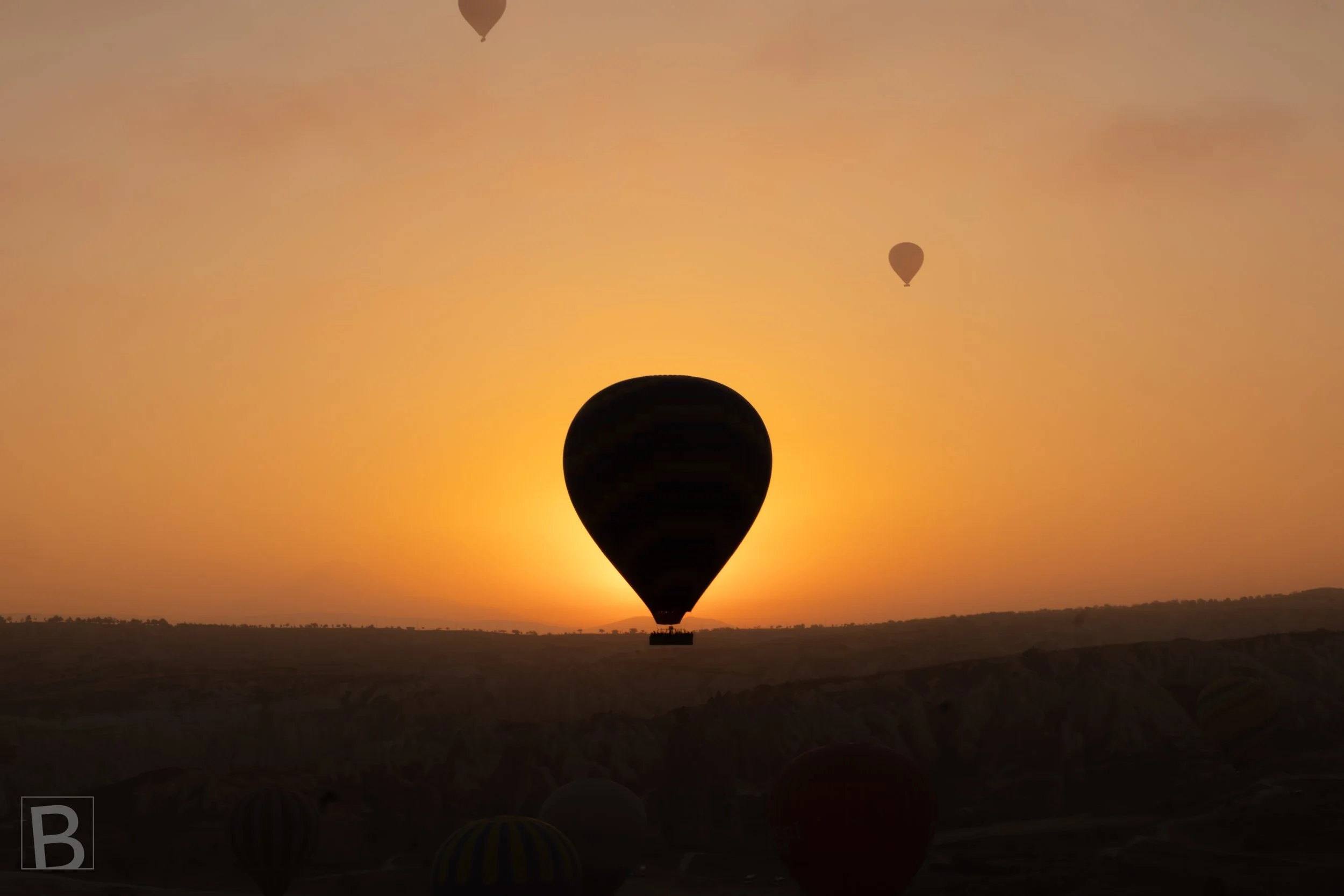 A hot air balloon crosses the glowing horizon at sunrise, creating a
simple silhouette against warm light and distant terrain. Cappadocia at sun break.