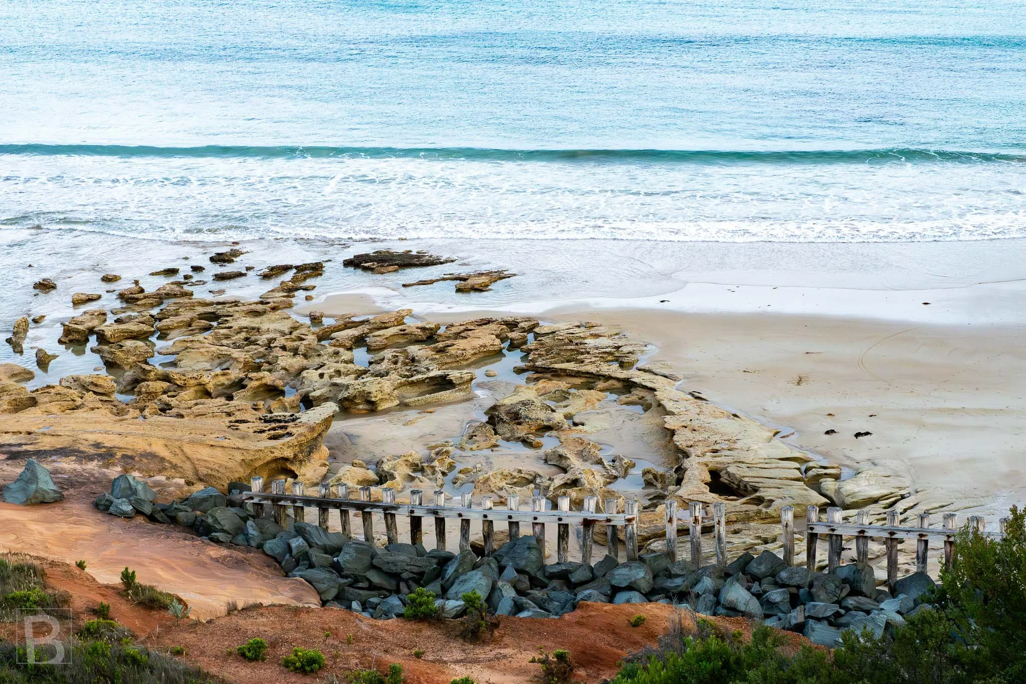Rock shelves and weathered coastal textures create subtle patterns
where sand, constructed edge and ocean meet.