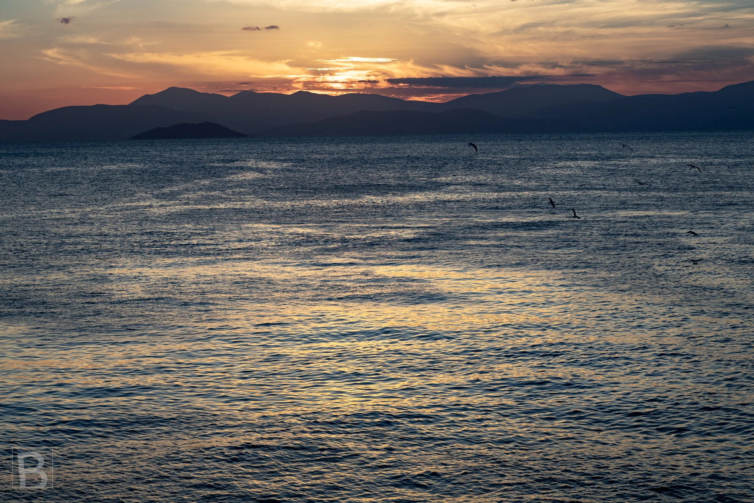 Warm sunset light settles over the sea and distant mountains in a
quiet landscape photograph shaped by colour, water and
atmosphere.