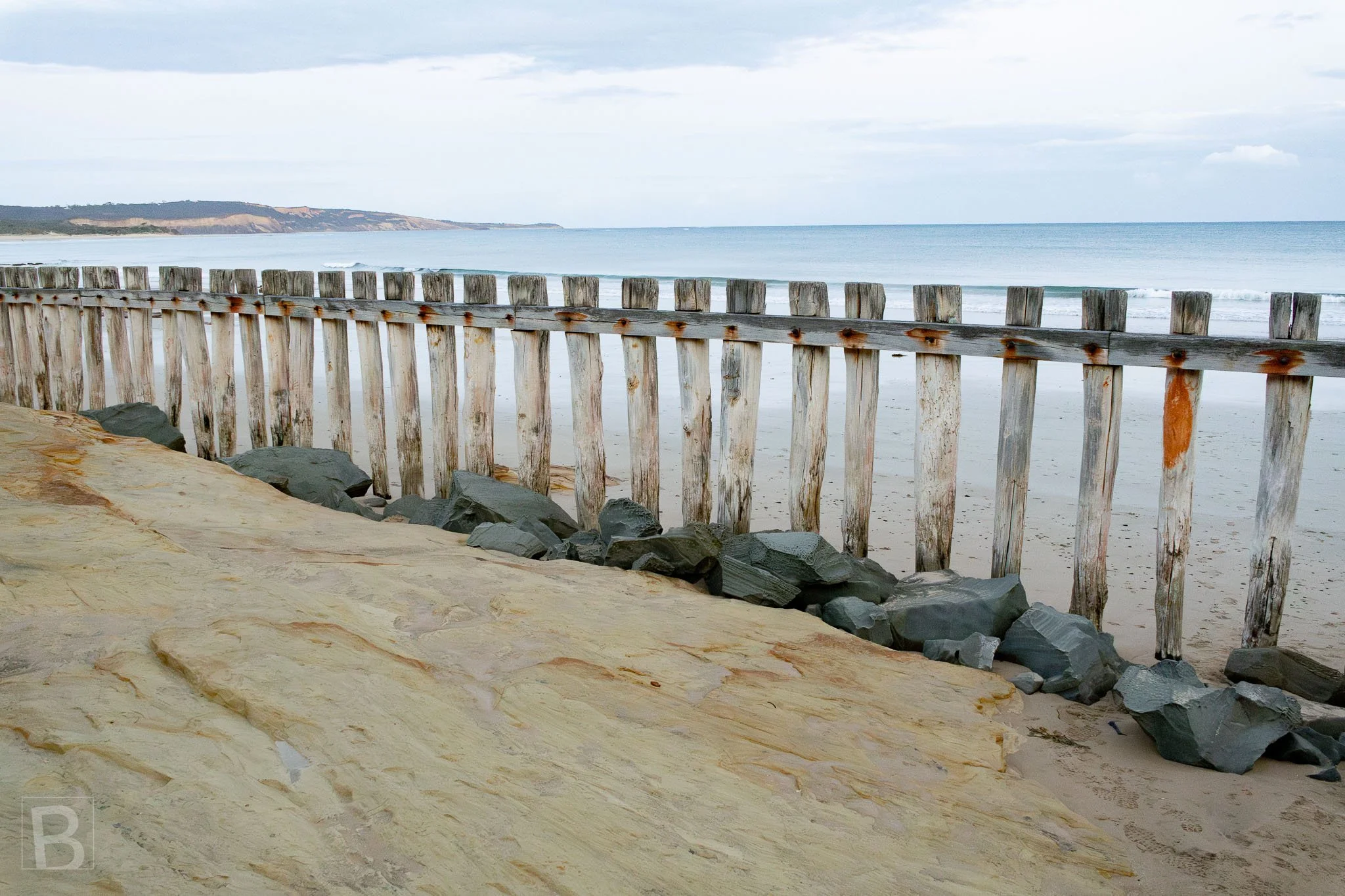 Timber, stone and sand meet along a constructed coastal edge,
showing the quiet infrastructure used to resist erosion and changing
tides.