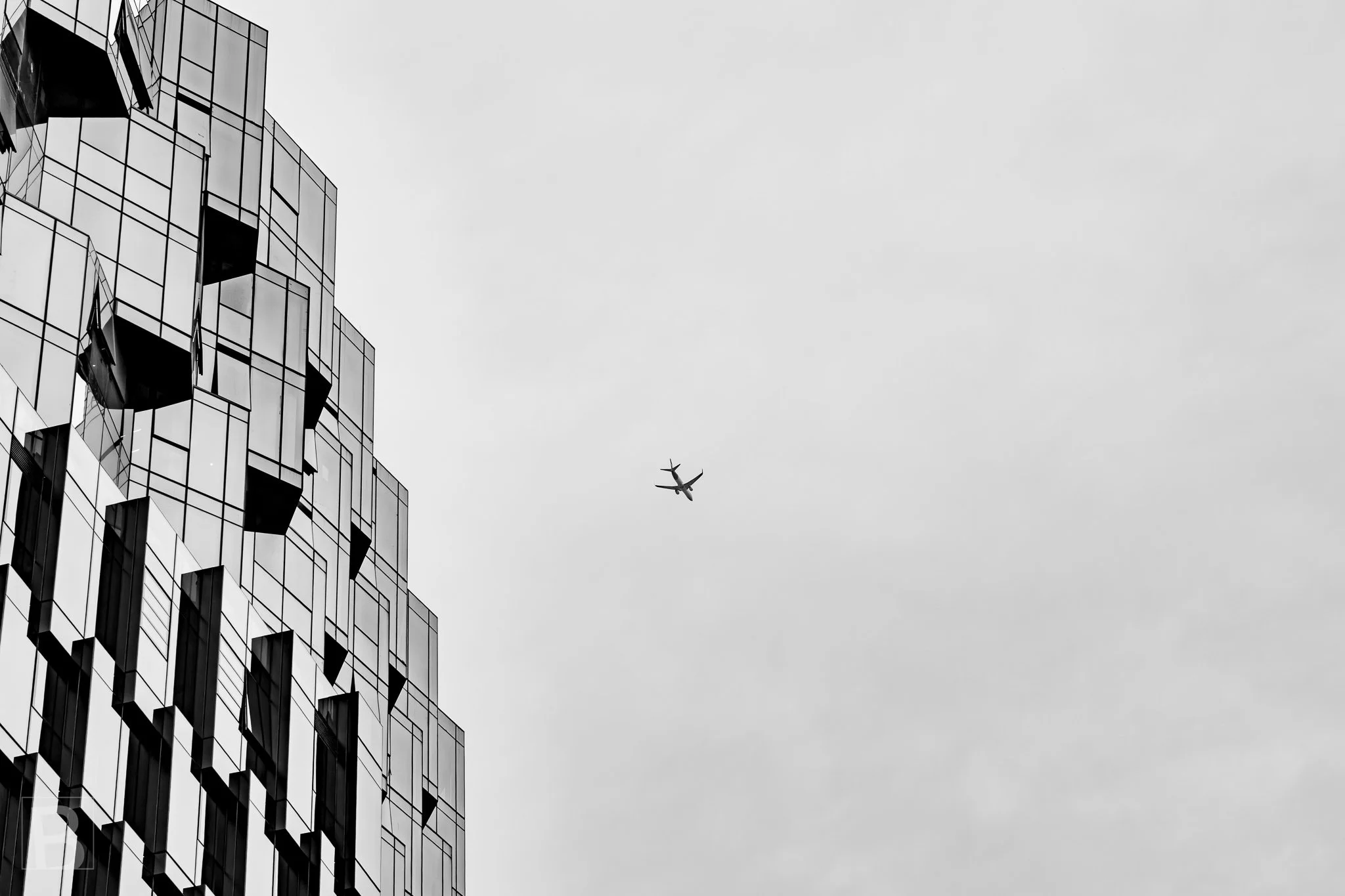 A passing plane adds scale and movement to a spare architectural
composition of fractured glass and empty sky.