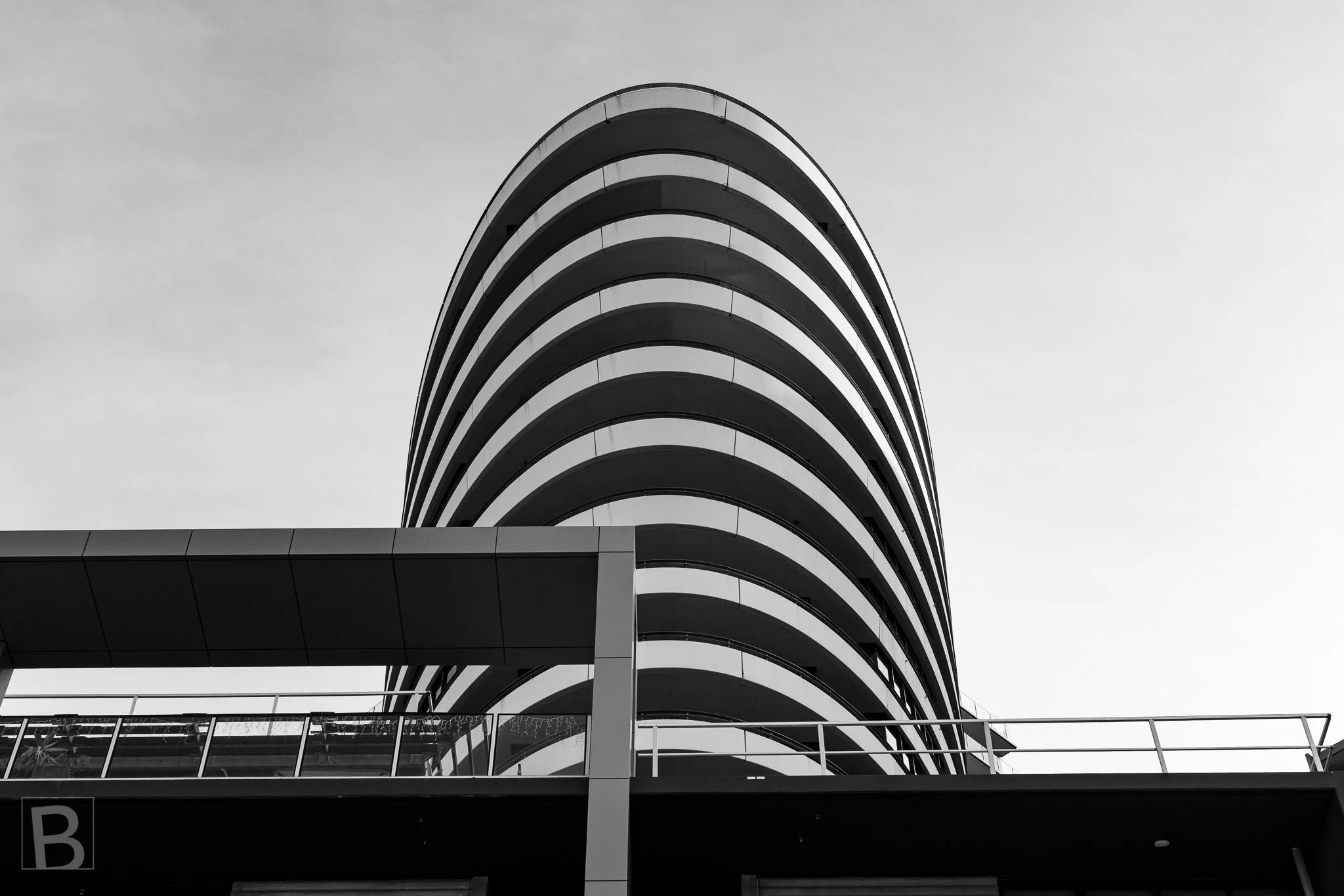 The tower's smooth oval profile and alternating dark balconies create
a strong vertical rhythm against a pale sky.